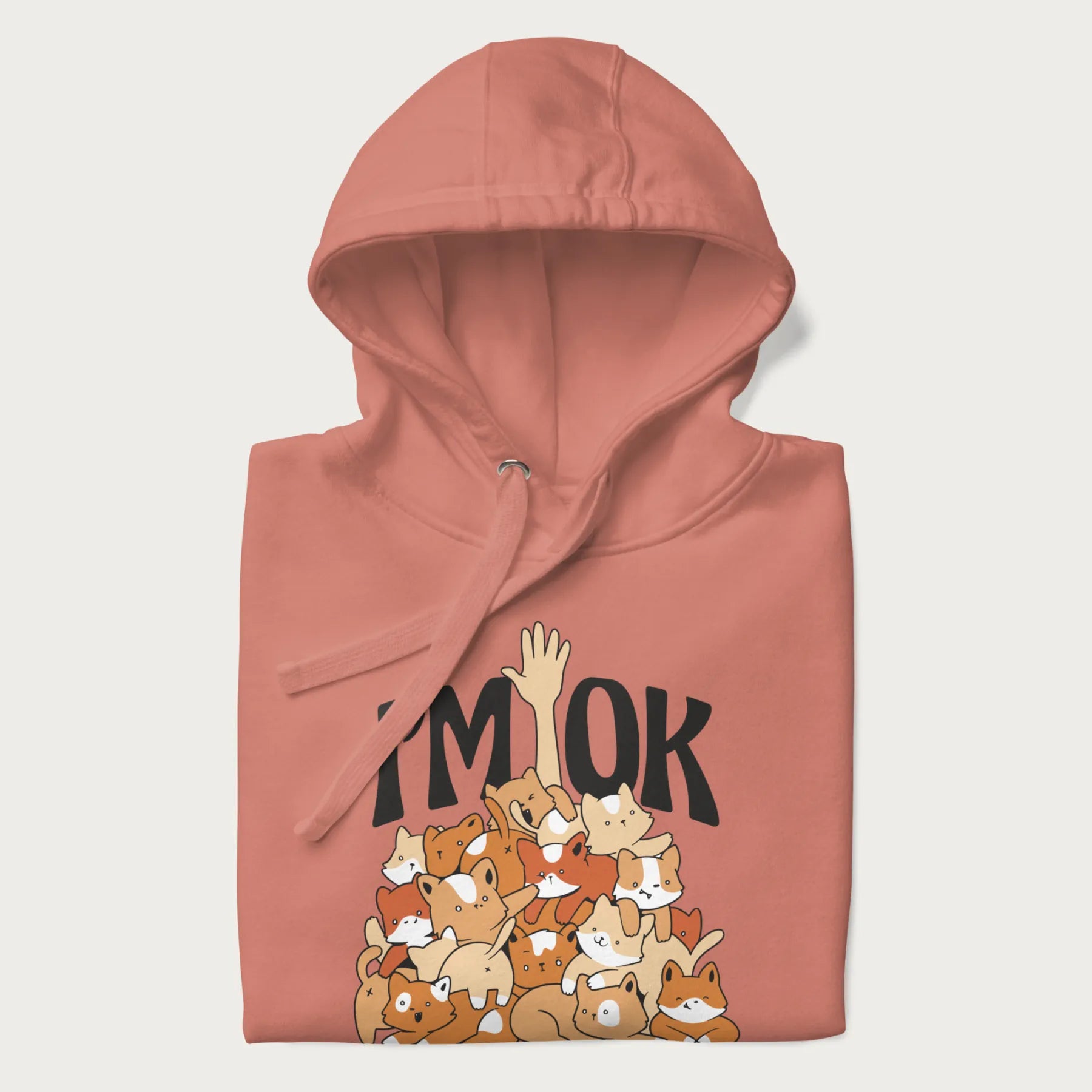 Folded light pink hoodie with a graphic of kittens piled on top of a person with "I'M OK" in large letters.