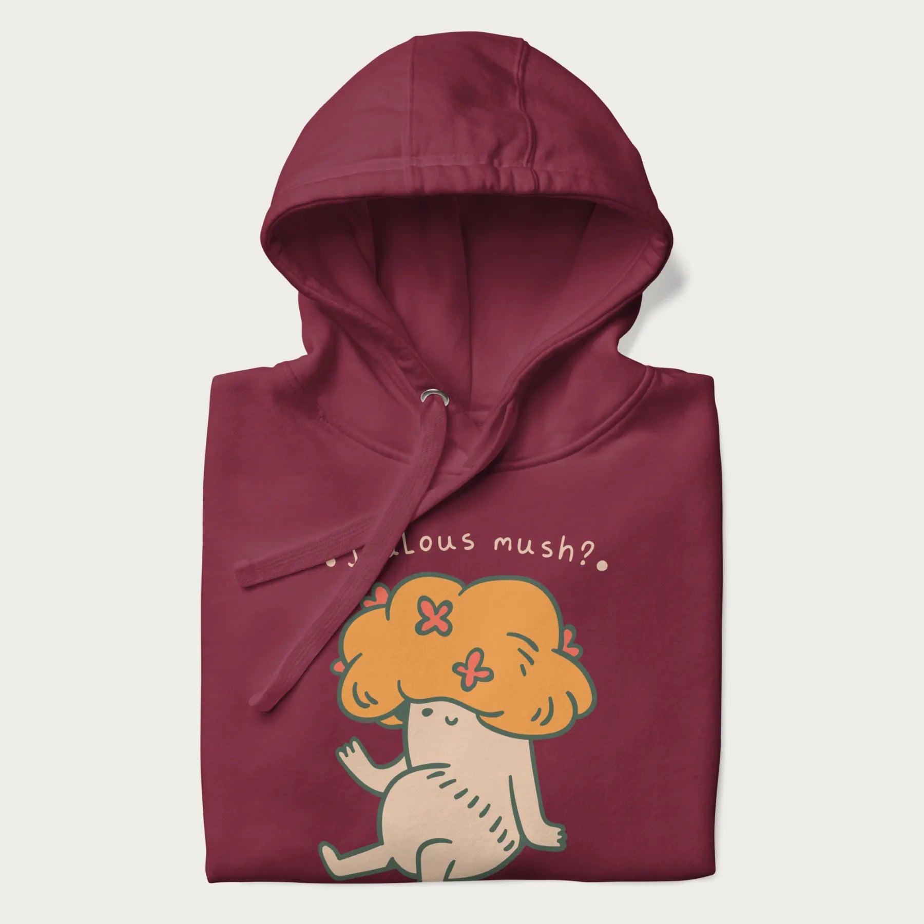 Folded maroon hoodie with a graphic of a mushroom character with an orange cap and the text 'Jealous mush?'.
