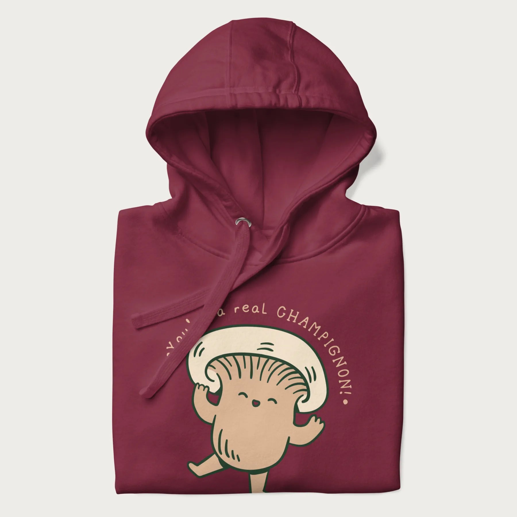 Folded maroon hoodie with a graphic of an adorable mushroom character and the text 'You're a real CHAMPIGNON!'.