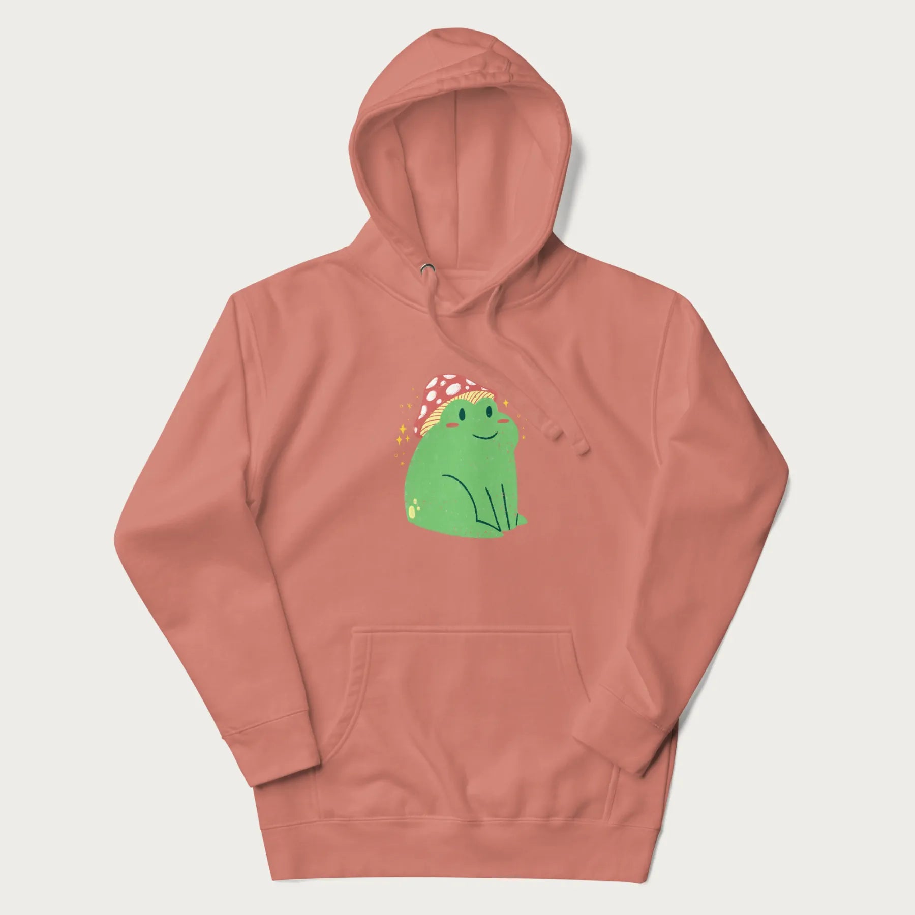 Light pink hoodie with a graphic of a green frog wearing a mushroom cap surrounded by stars.