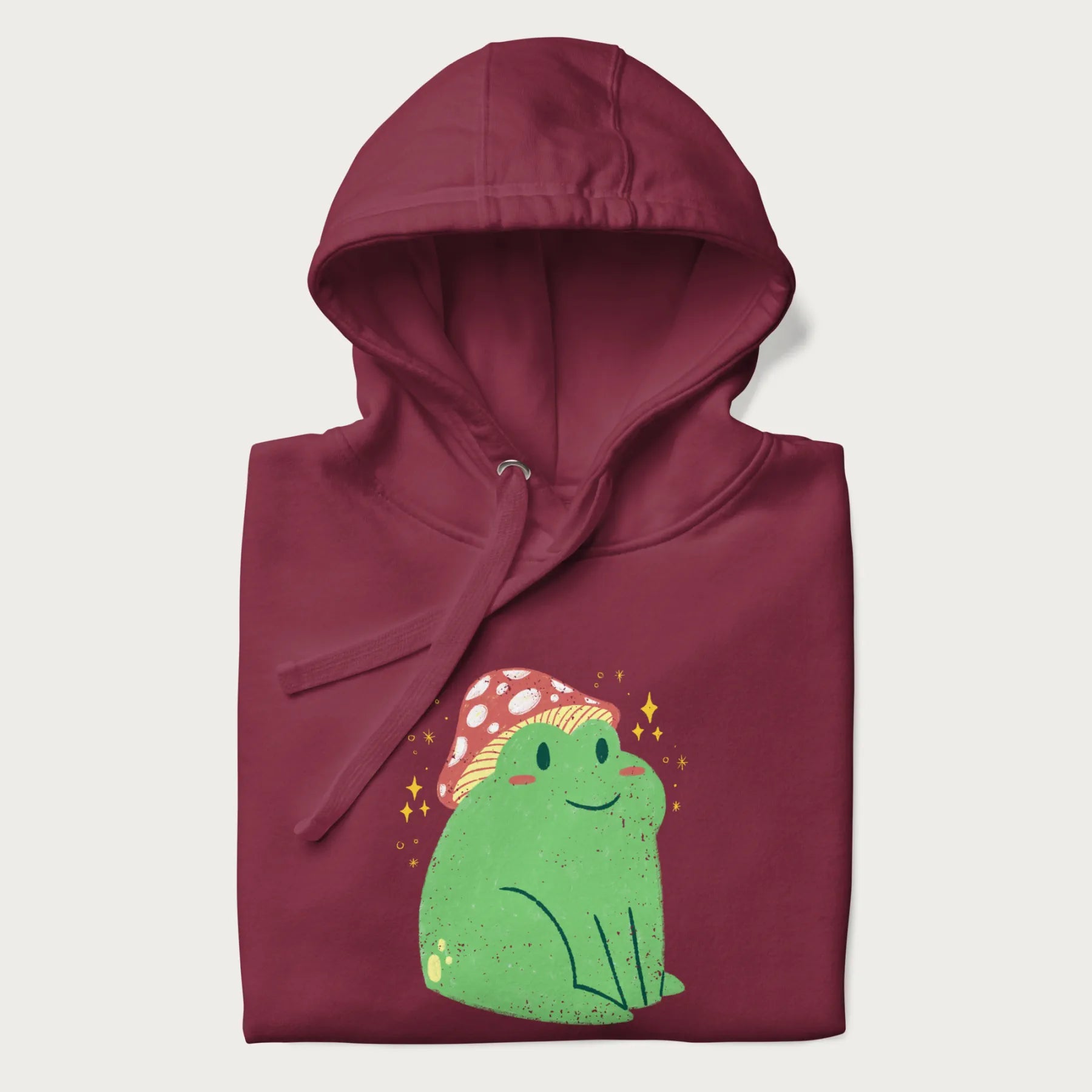Folded maroon hoodie with a graphic of a green frog wearing a mushroom cap surrounded by stars.