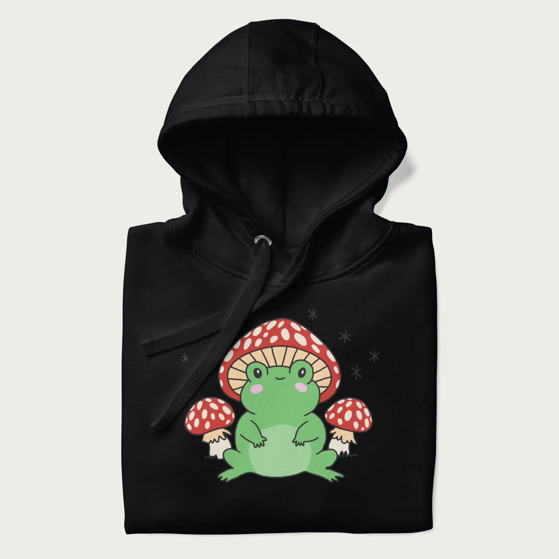 Black hoodie will illustration of a cute green frog with red and white mushrooms.