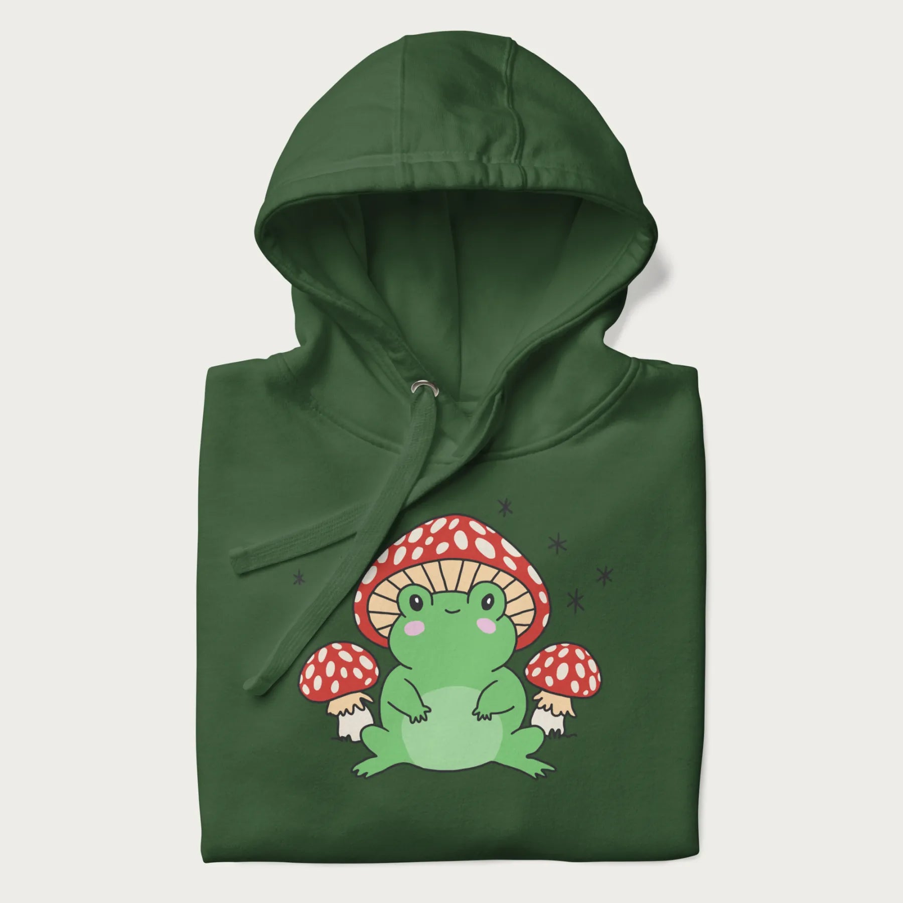 Folded forest green hoodie will illustration of a cute green frog with red and white mushrooms.