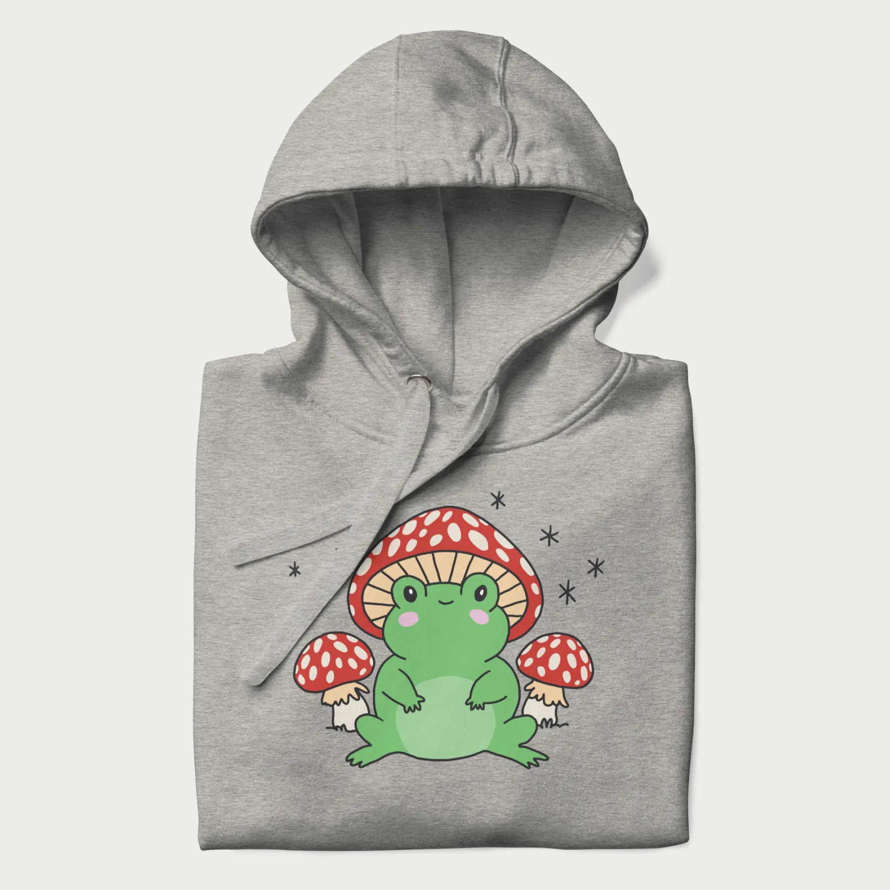 Folded light grey hoodie will illustration of a cute green frog with red and white mushrooms.