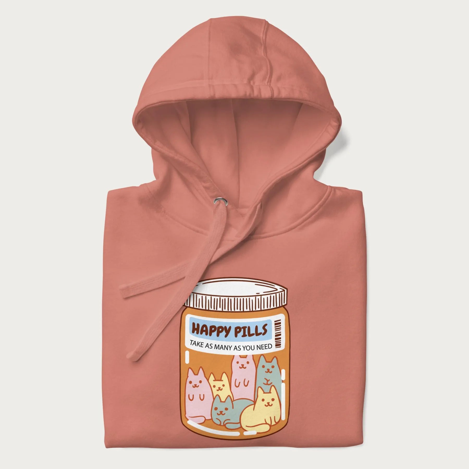 Cartoon cats in a pill bottle labeled 'Happy Pills' on a folded light pink hoodie.
