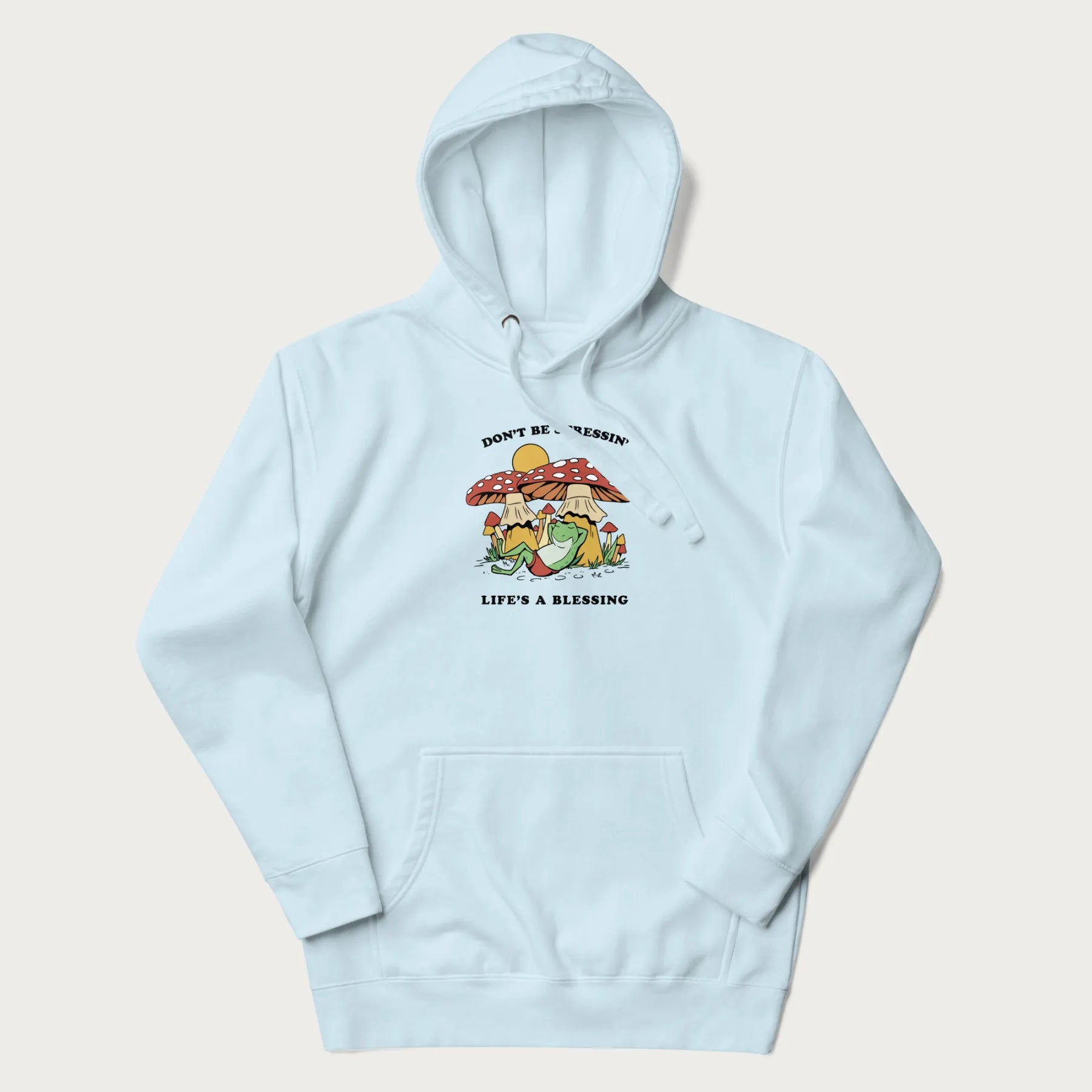 Light blue hoodie with a graphic of a frog lounging under mushrooms and the phrases 'Don't Be Stressin' Life's a Blessing'.