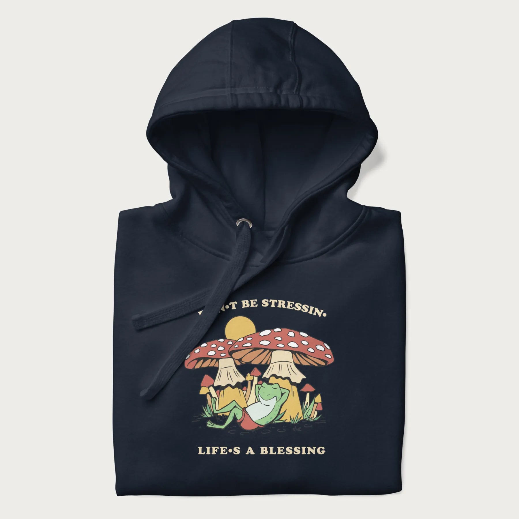 Folded navy blue hoodie with a graphic of a frog lounging under mushrooms and the phrases 'Don't Be Stressin' Life's a Blessing'.