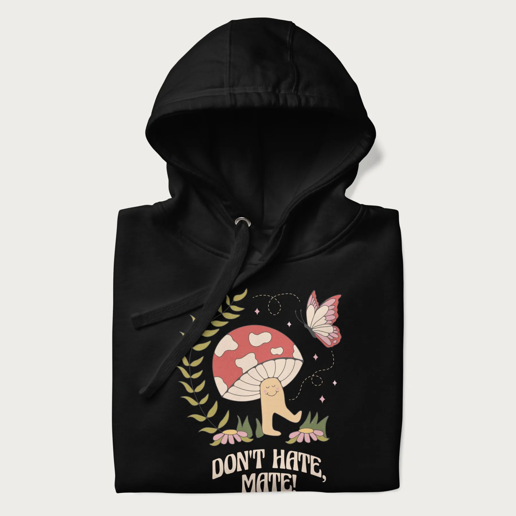 Folded black hoodie featuring a cute mushroom graphic with the text "Don't Hate, Mate."