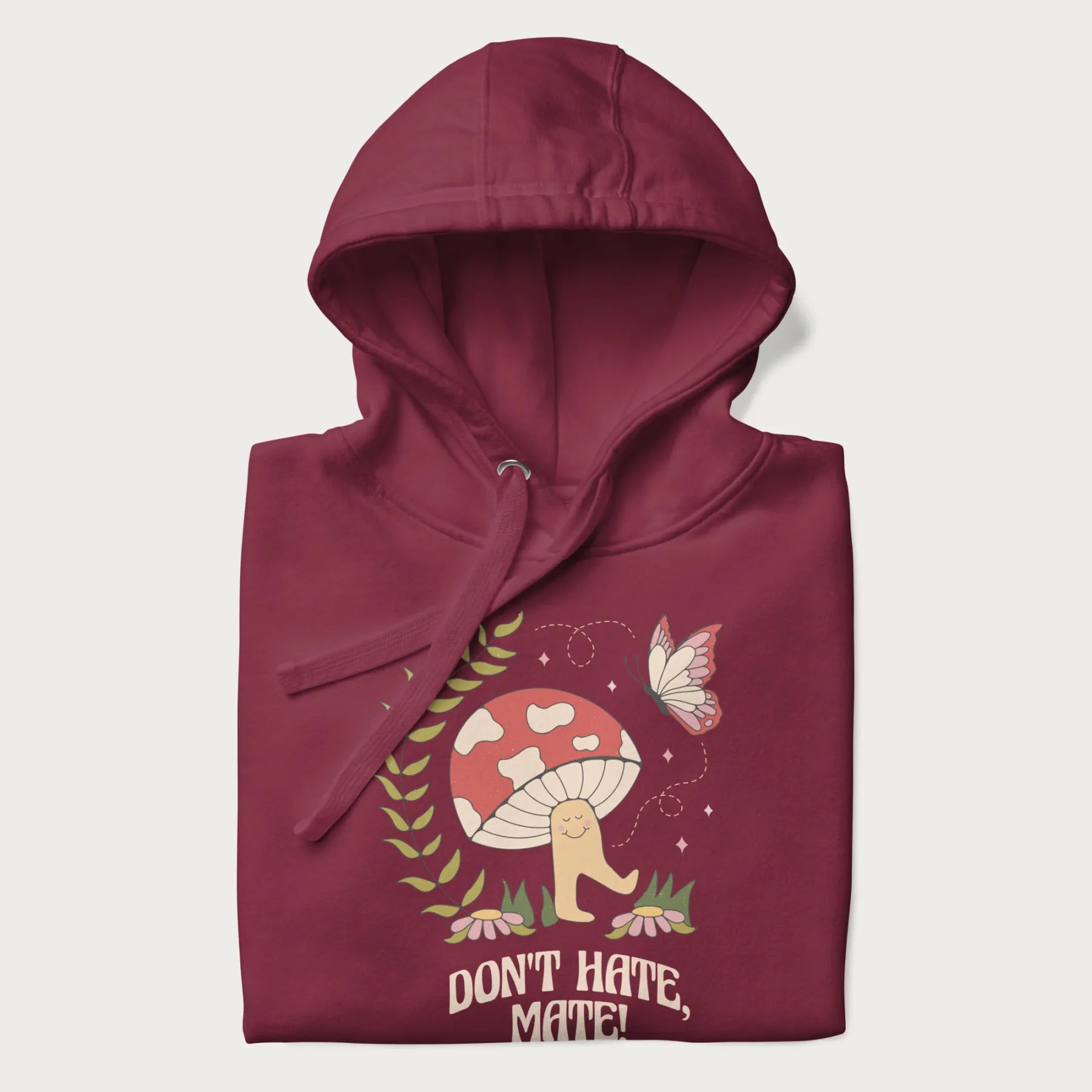 Folded maroon hoodie featuring a cute mushroom graphic with the text "Don't Hate, Mate."