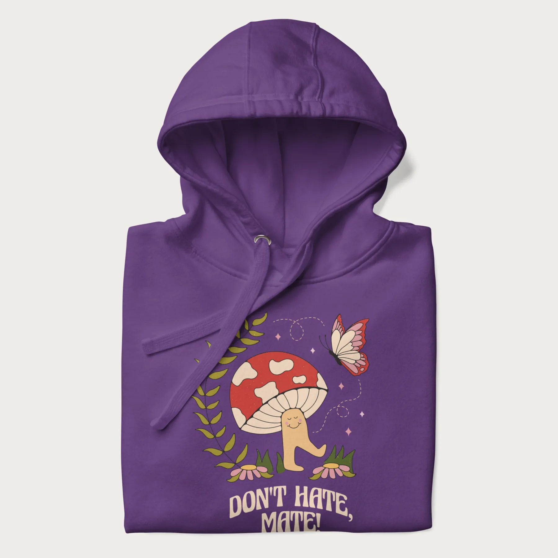 Folded purple hoodie featuring a cute mushroom graphic with the text "Don't Hate, Mate."