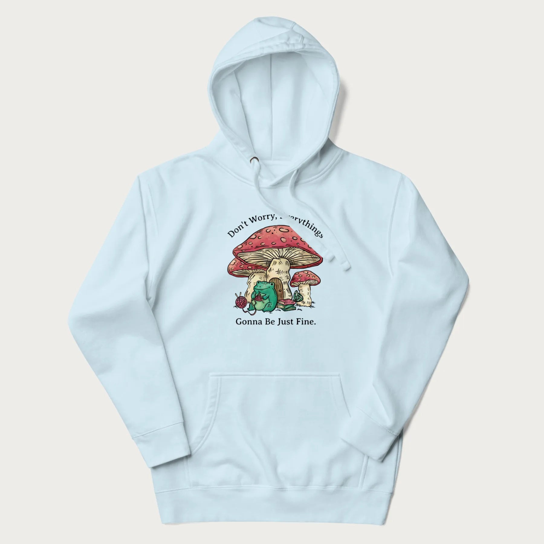 Light blue hoodie with a graphic of a frog knitting under a large mushroom with the text 'Don't Worry, Everything's Gonna Be Just Fine'.