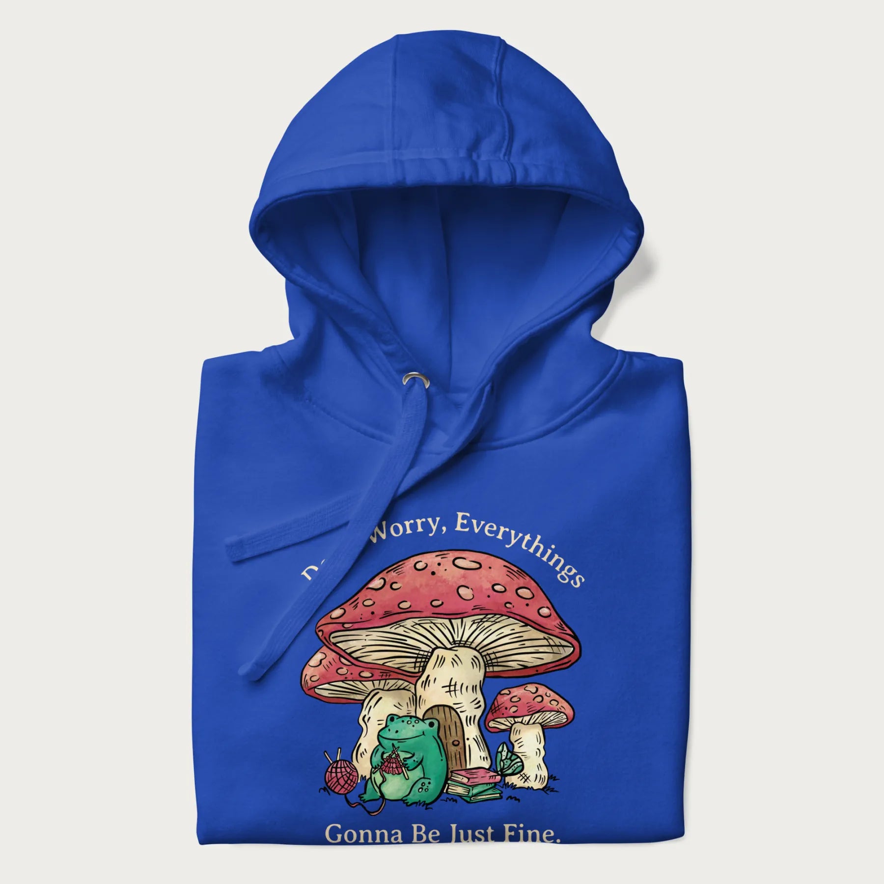Folded royal blue hoodie with a graphic of a frog knitting under a large mushroom with the text 'Don't Worry, Everything's Gonna Be Just Fine'.