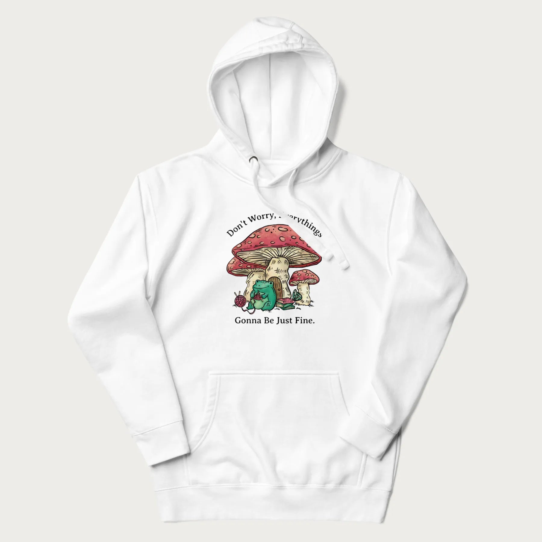 White hoodie with a graphic of a frog knitting under a large mushroom with the text 'Don't Worry, Everything's Gonna Be Just Fine'.