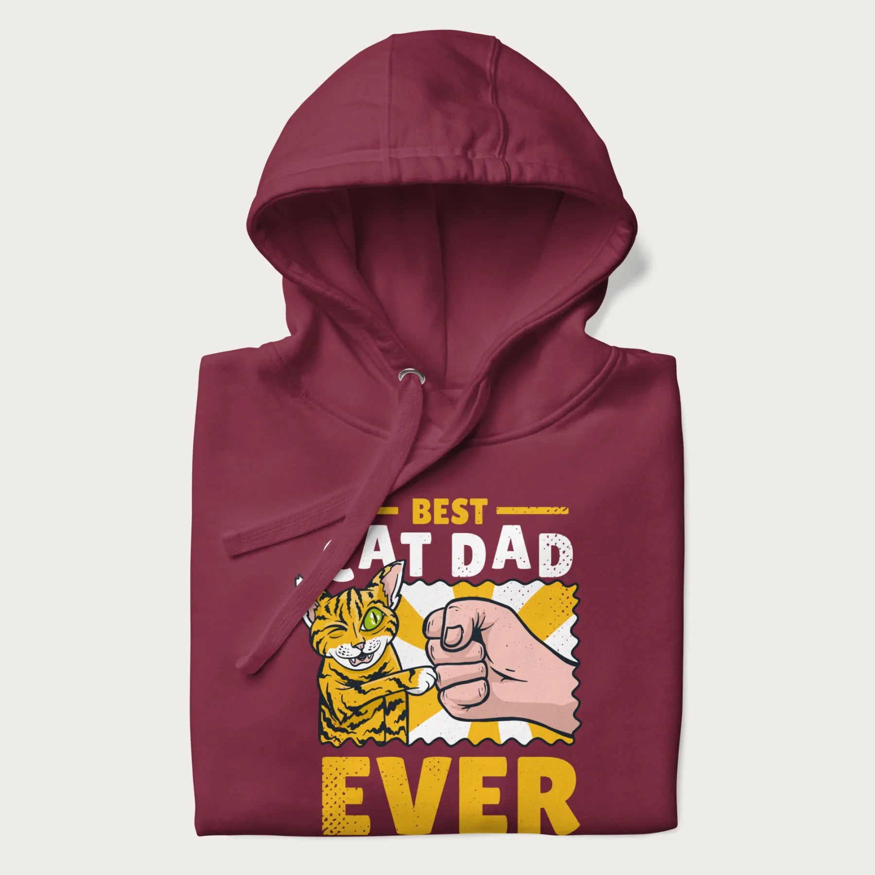 Folded maroon hoodie with a graphic of a tabby cat and a human fist bumping, with 'Best Cat Dad Ever' in bold letters.