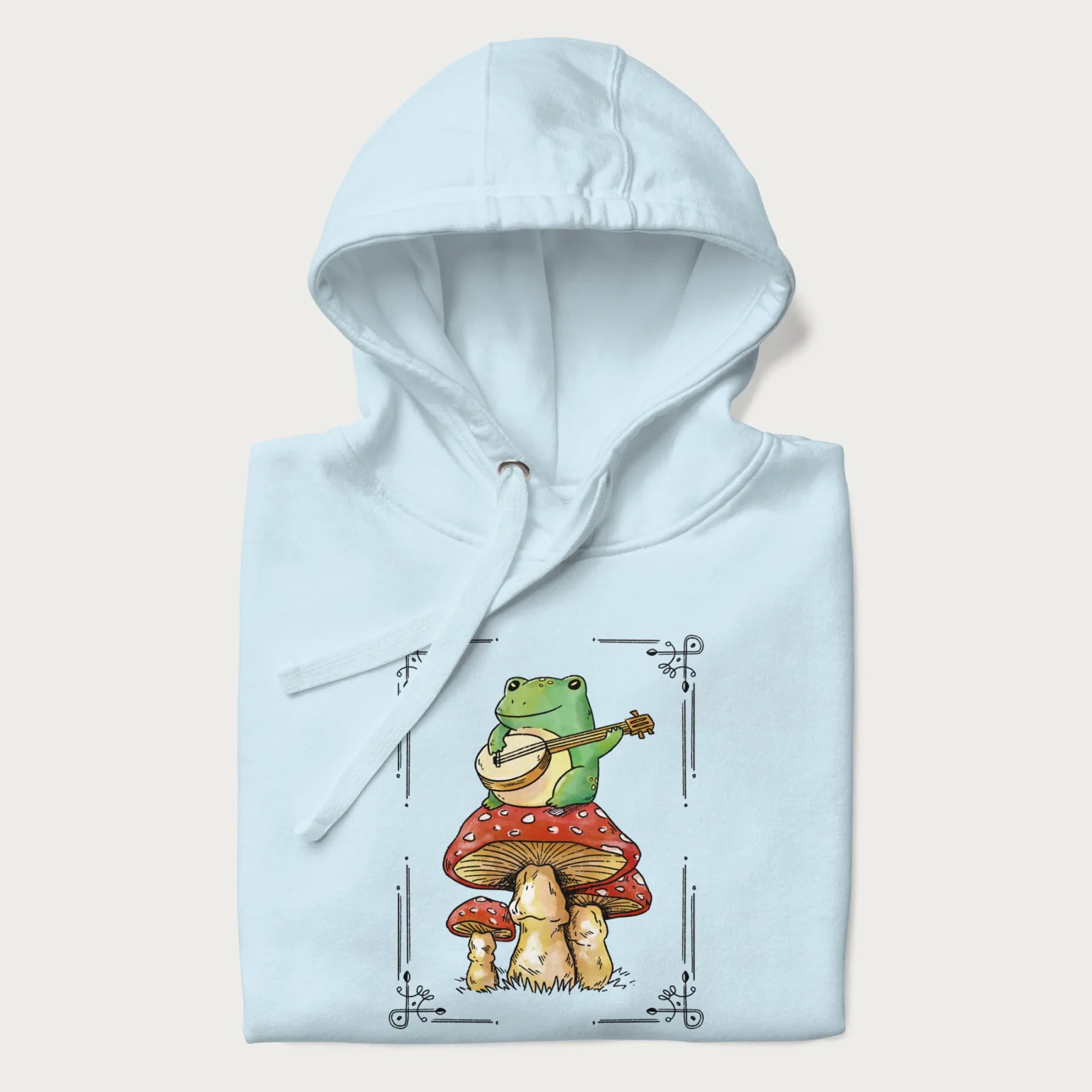 Folded light blue hoodie featuring a graphic of a frog playing a banjo on top of red mushrooms.