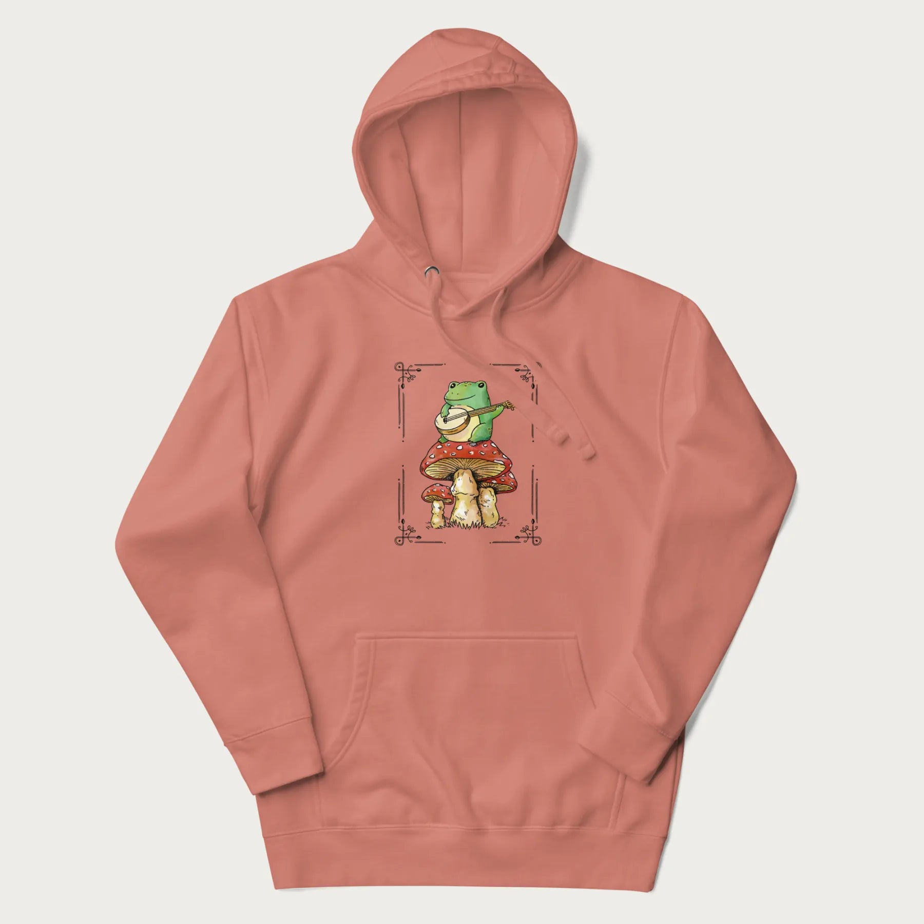Light pink hoodie featuring a graphic of a frog playing a banjo on top of red mushrooms.