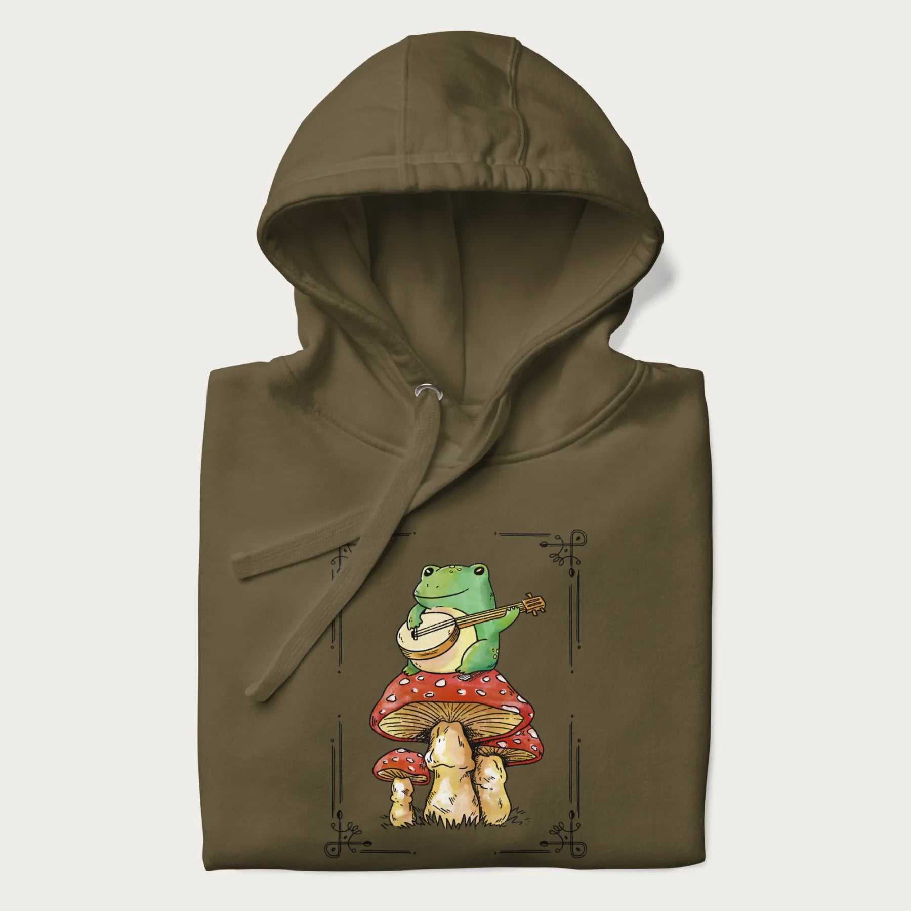 Folded military green hoodie featuring a graphic of a frog playing a banjo on top of red mushrooms.