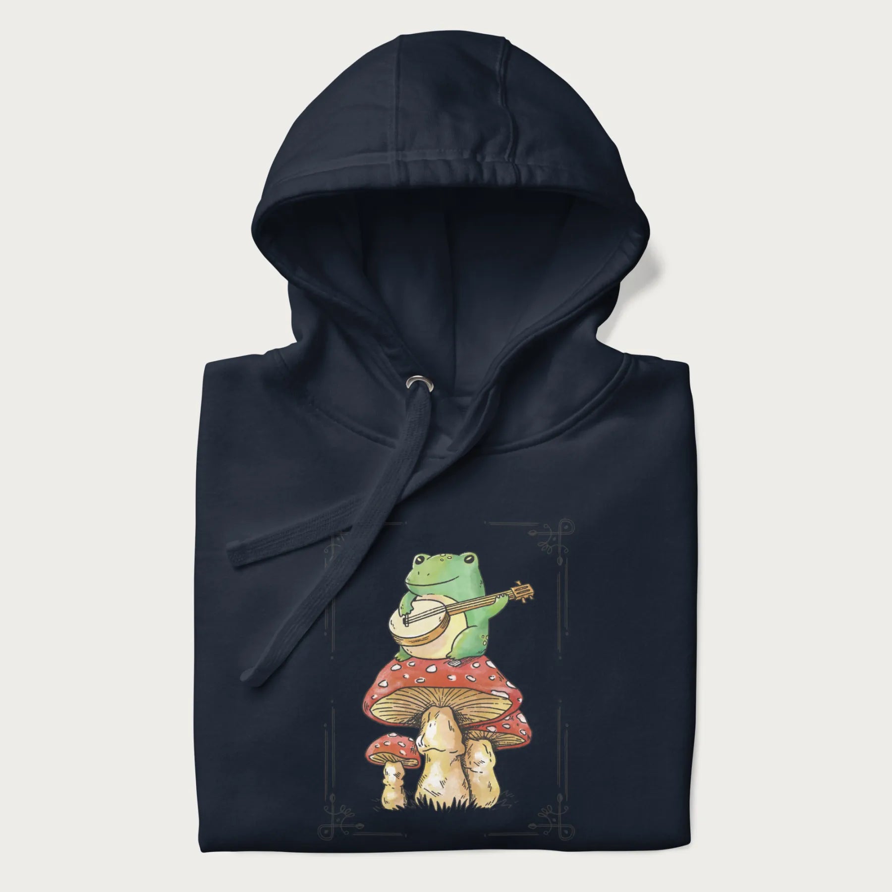 Folded navy blue hoodie featuring a graphic of a frog playing a banjo on top of red mushrooms.