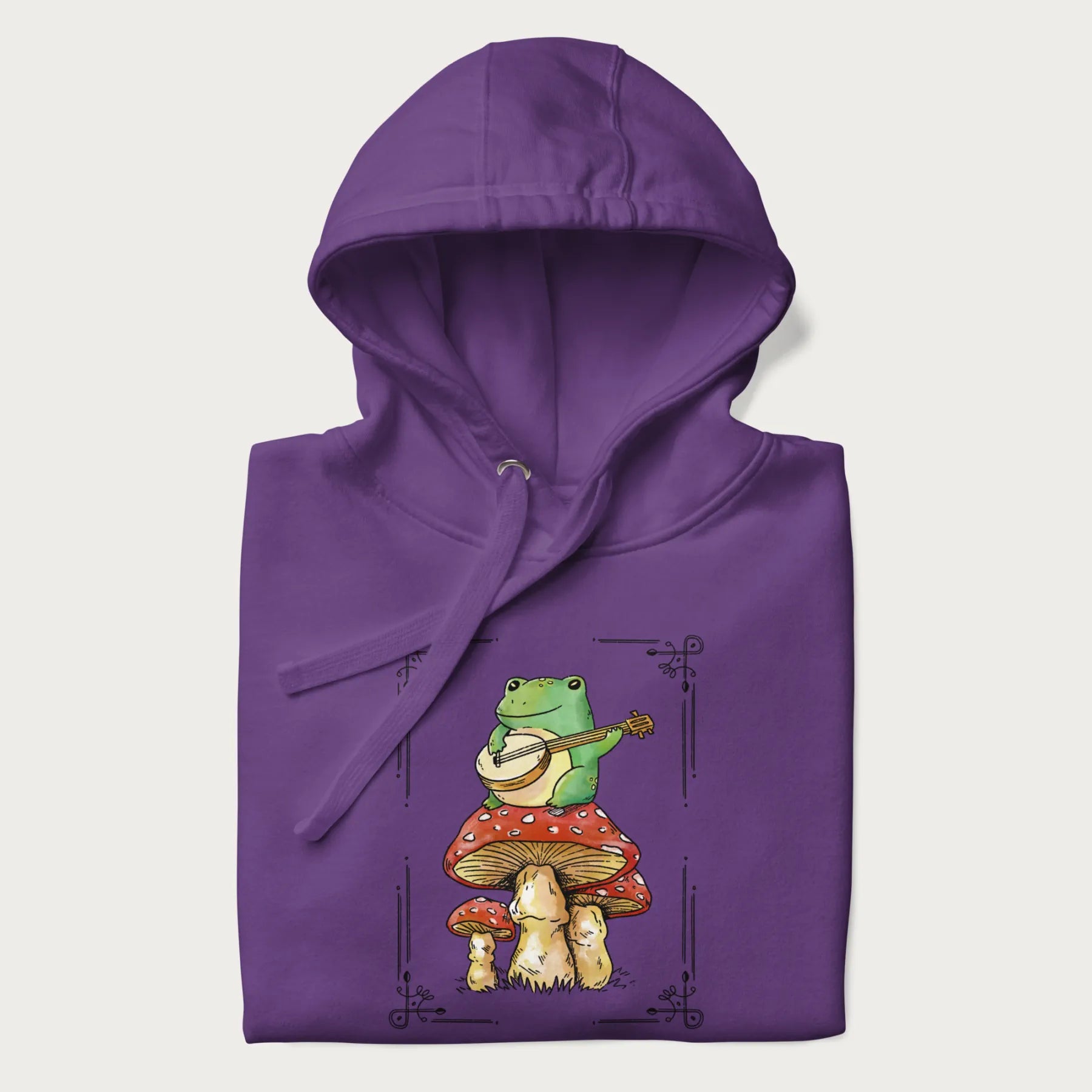 Folded purple hoodie featuring a graphic of a frog playing a banjo on top of red mushrooms.