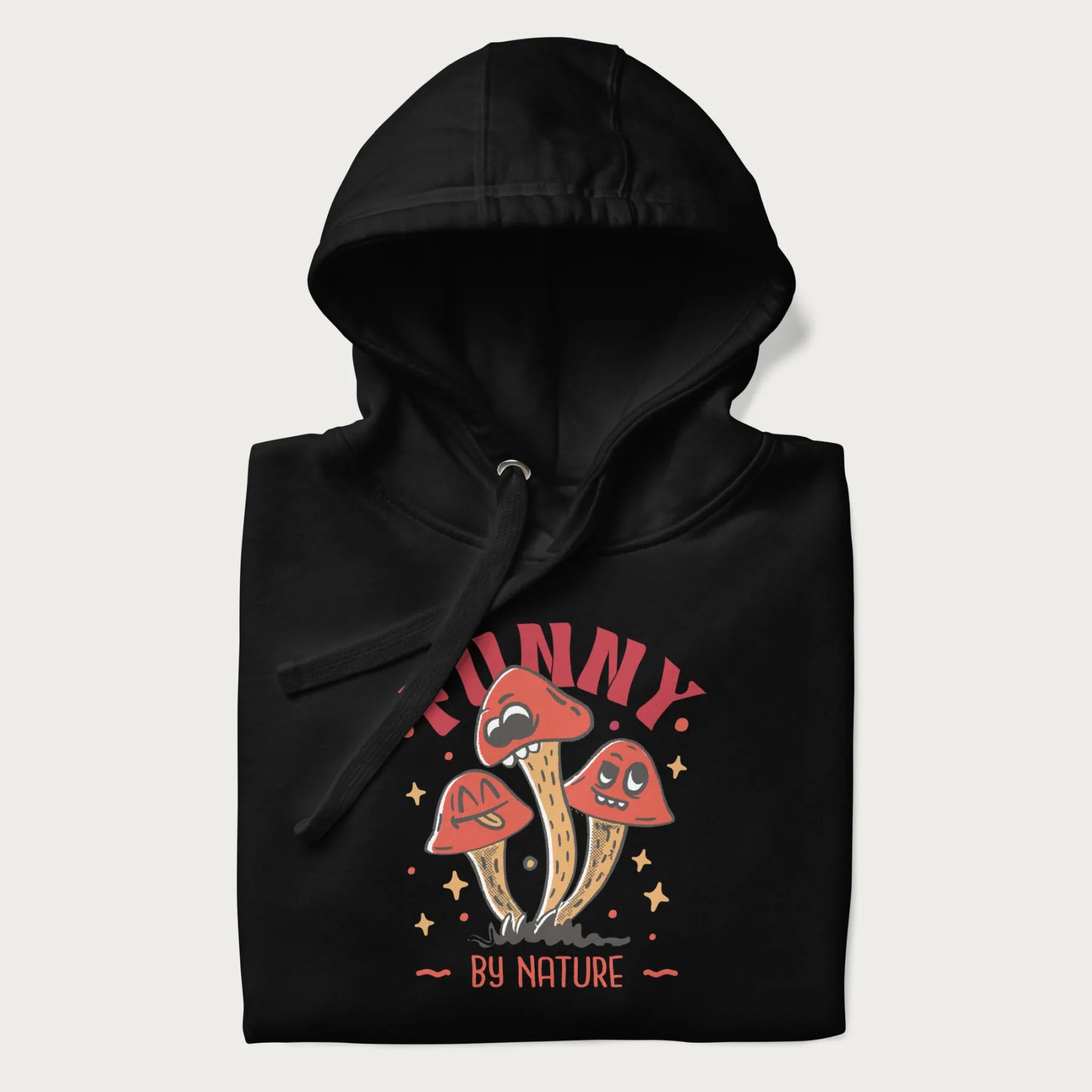 Folded black hoodie featuring a playful graphic of three mushrooms with expressive faces and the text "Funny by Nature."