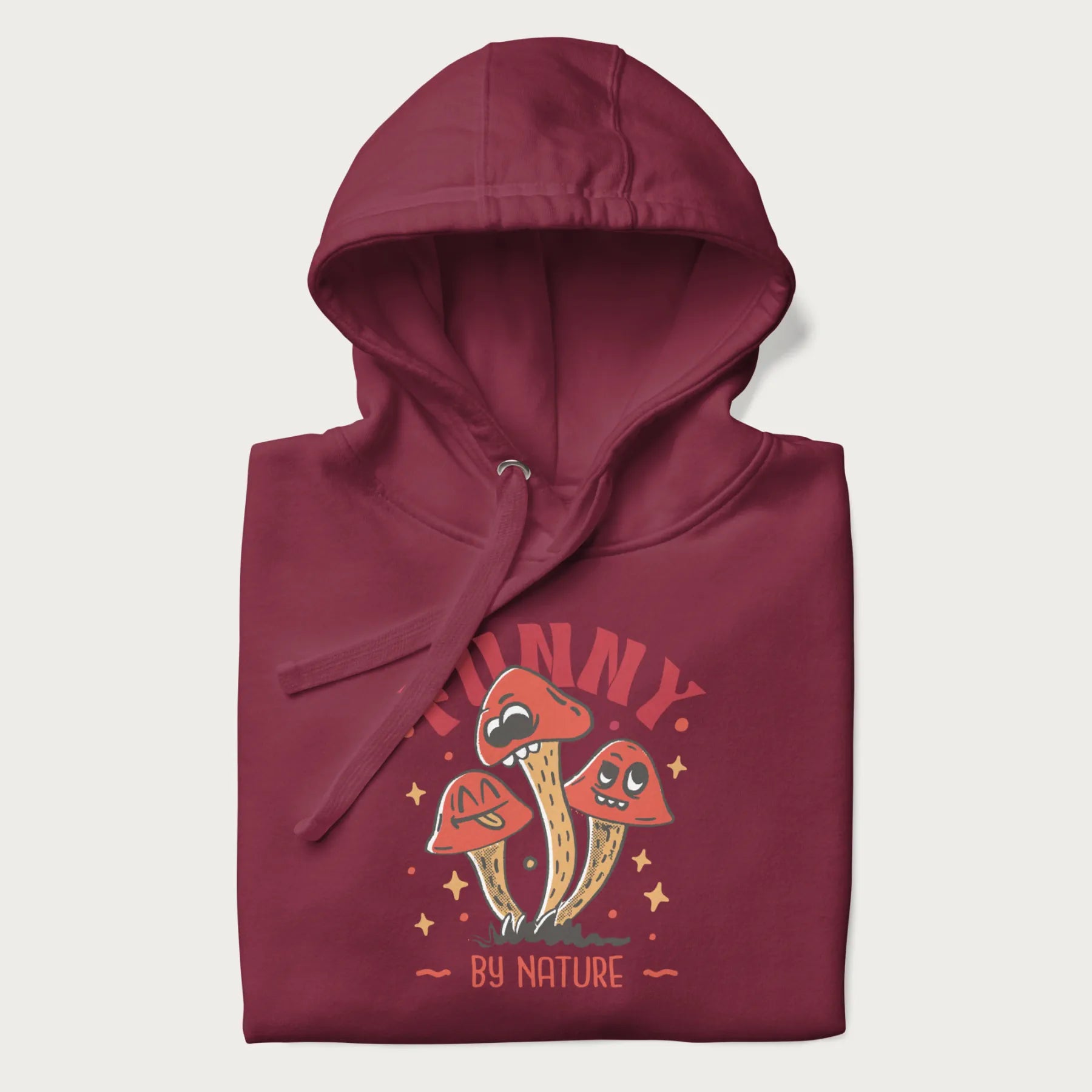 Folded maroon hoodie featuring a playful graphic of three mushrooms with expressive faces and the text "Funny by Nature."