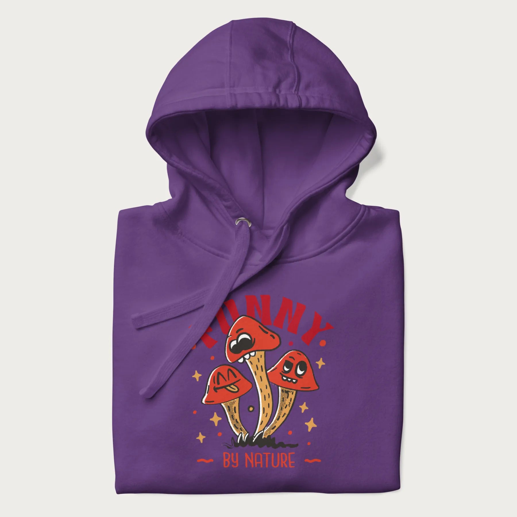 Folded purple hoodie featuring a playful graphic of three mushrooms with expressive faces and the text "Funny by Nature."