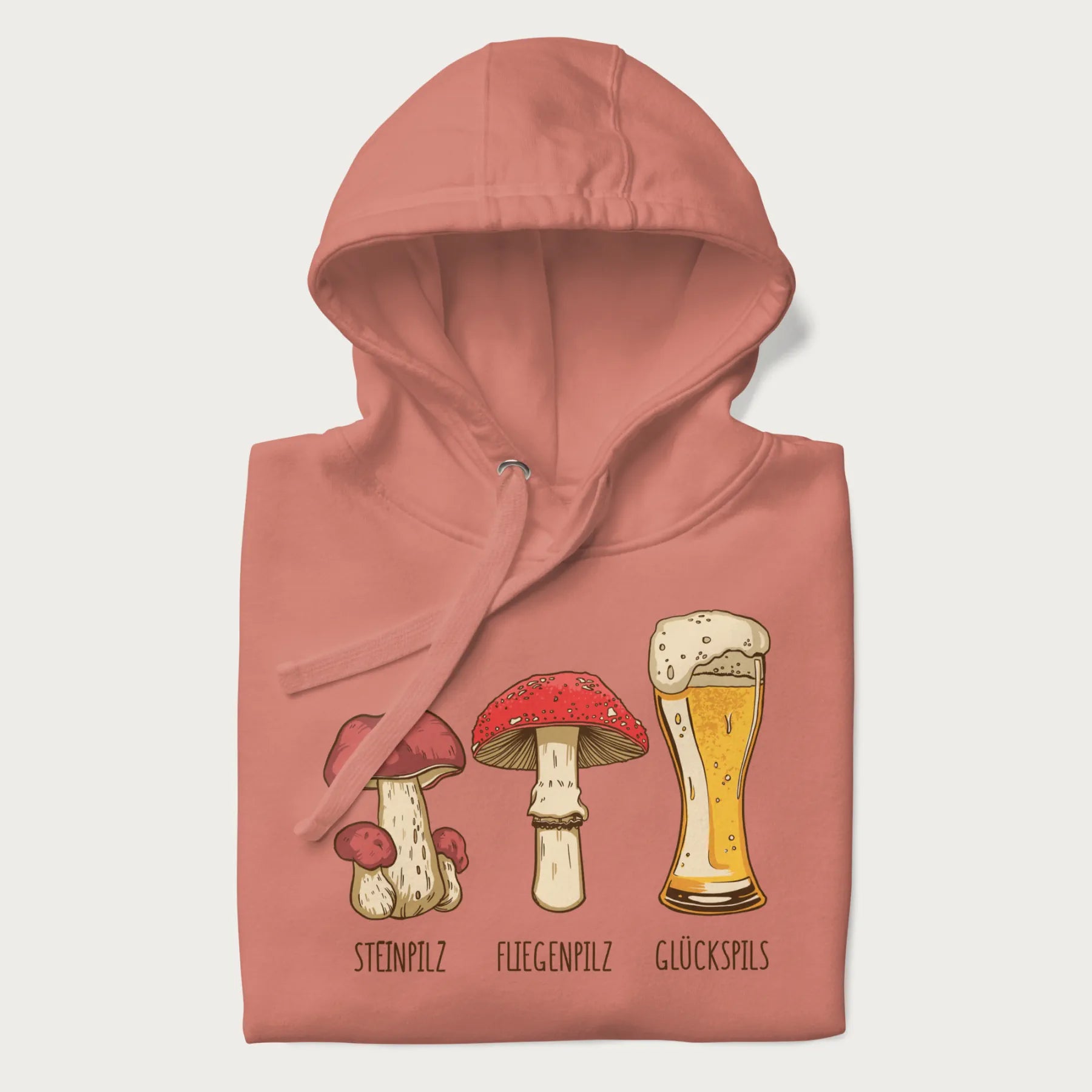 Folded light pink hoodie with illustrations of a Steinpilz, Fliegenpilz, and a beer glass labeled Glückspils.