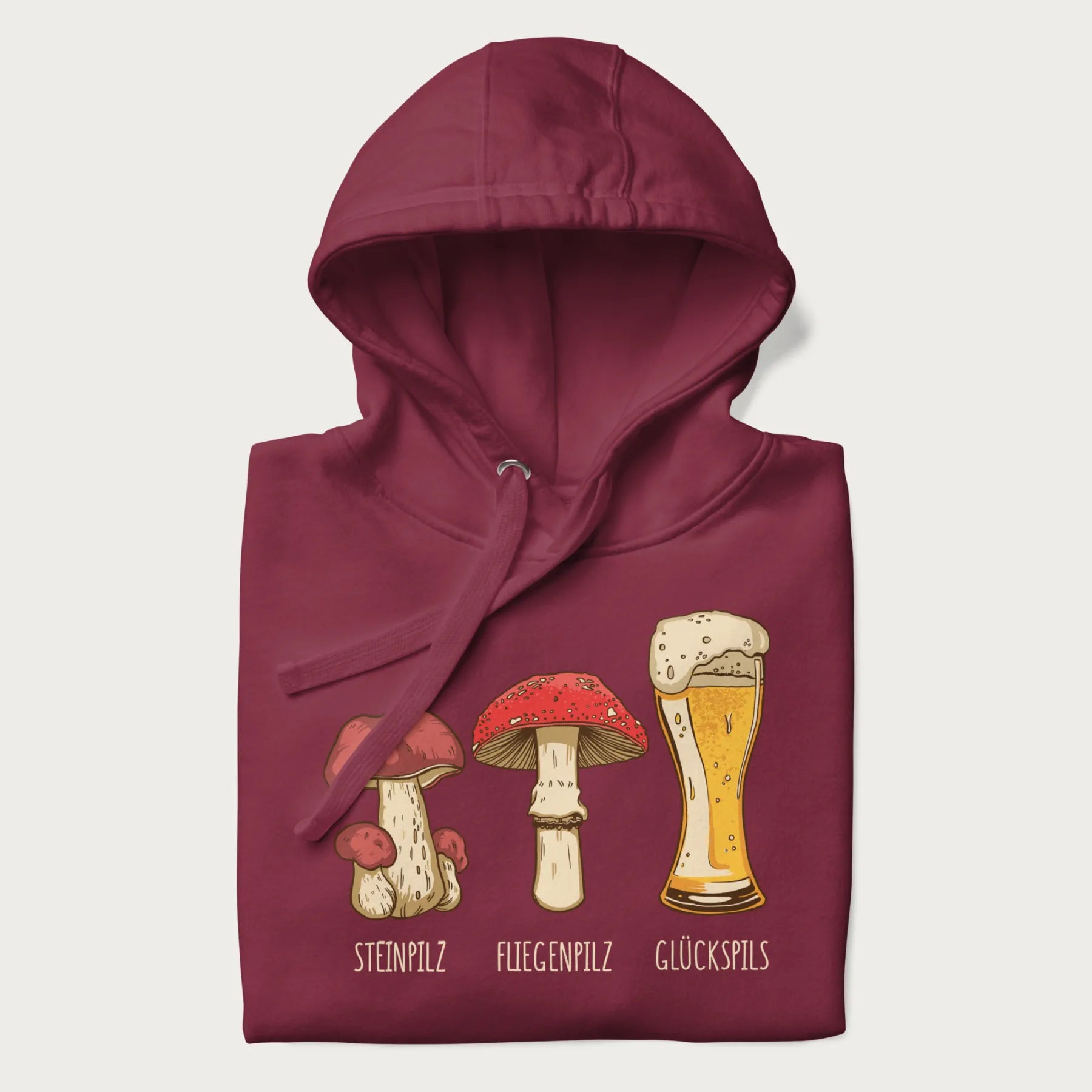 Folded maroon hoodie with illustrations of a Steinpilz, Fliegenpilz, and a beer glass labeled Glückspils.