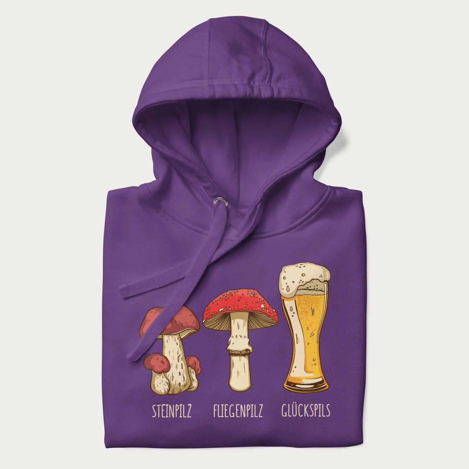 Folded purple hoodie with illustrations of a Steinpilz, Fliegenpilz, and a beer glass labeled Glückspils.