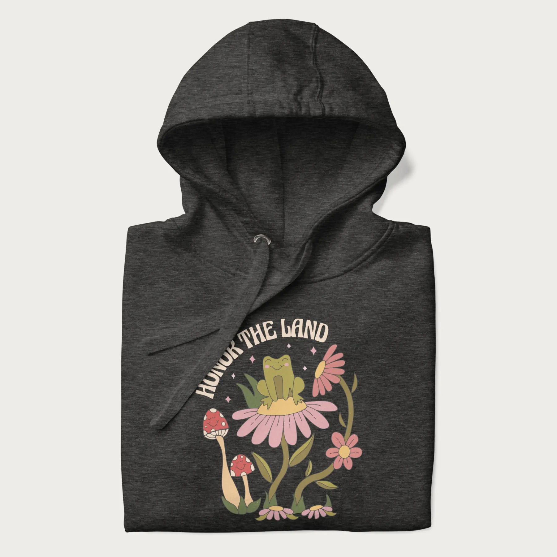 Folded dark grey hoodie with a graphic of a frog sitting on a flower, surrounded by mushrooms and flowers, with the text 'Honor the Land'.