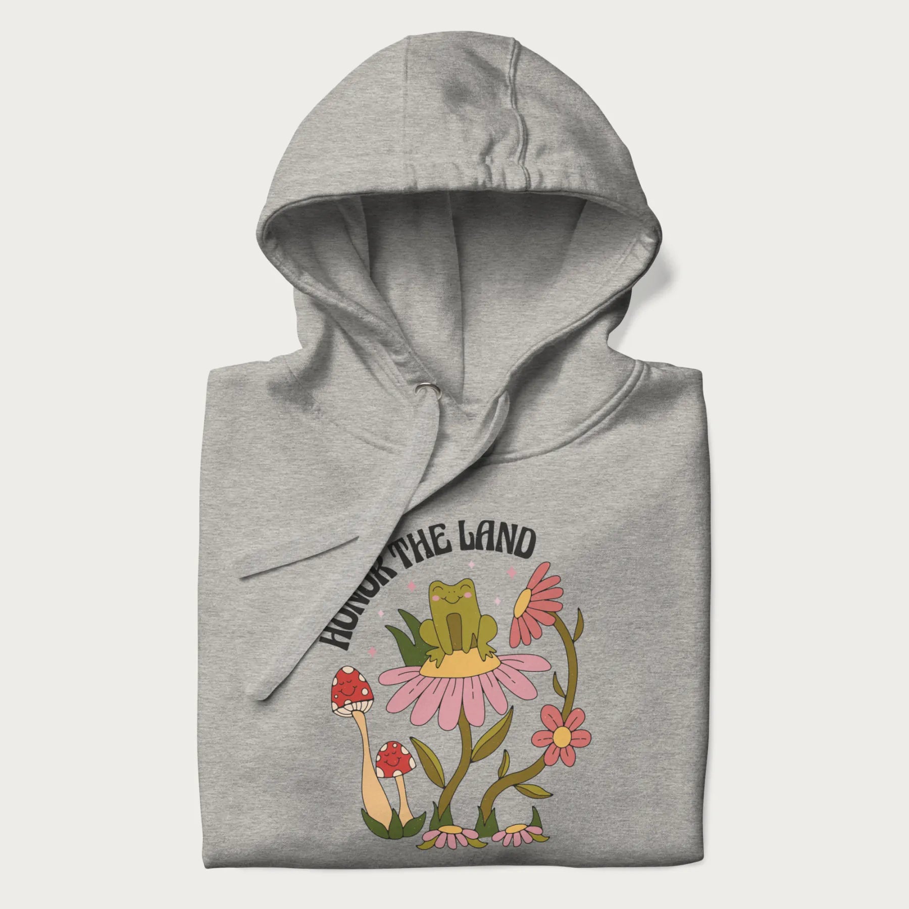 Folded light grey hoodie with a graphic of a frog sitting on a flower, surrounded by mushrooms and flowers, with the text 'Honor the Land'.