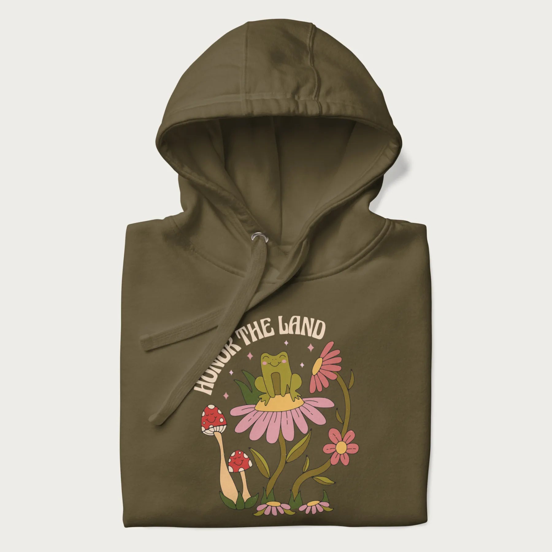Folded military green hoodie with a graphic of a frog sitting on a flower, surrounded by mushrooms and flowers, with the text 'Honor the Land'.