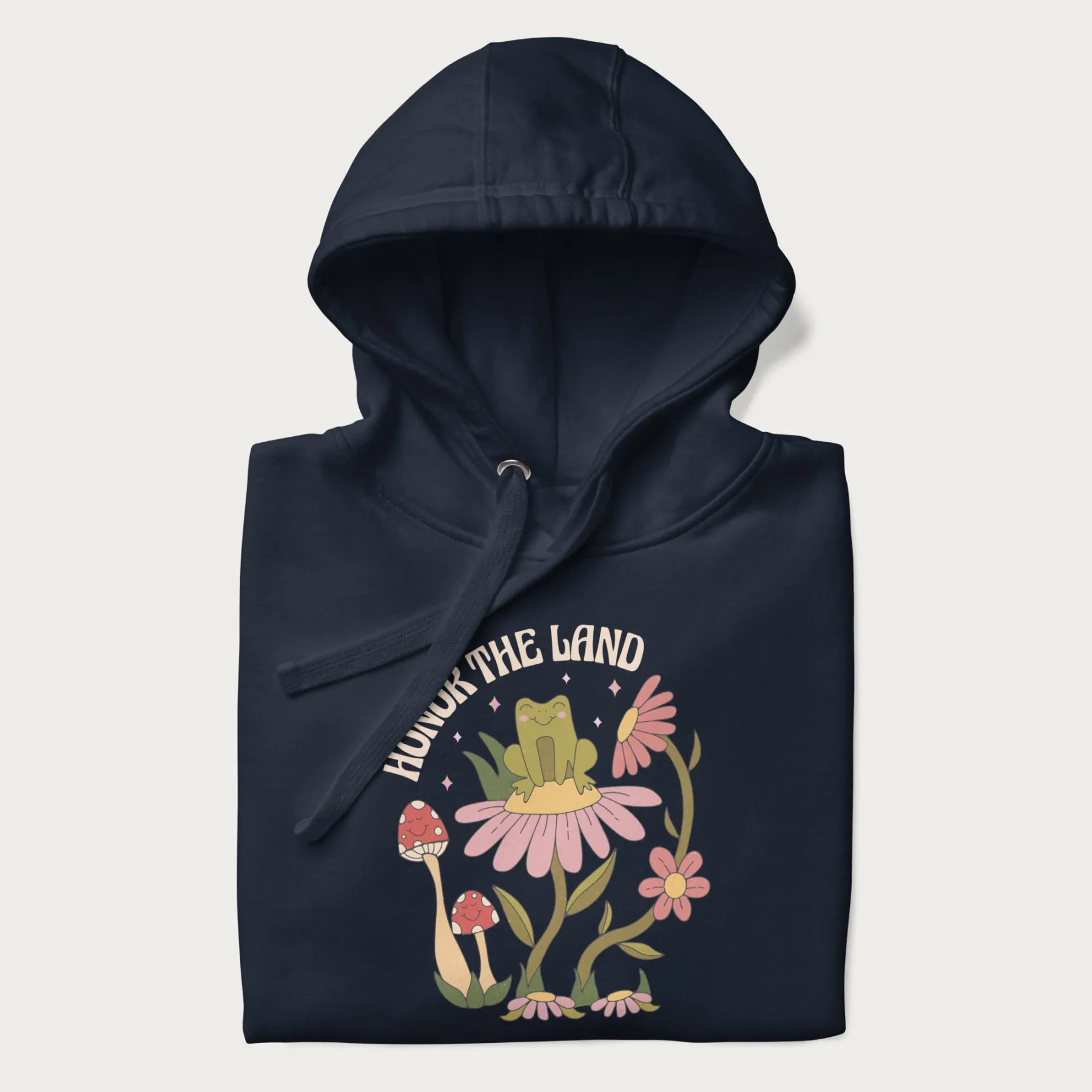 Folded navy blue hoodie with a graphic of a frog sitting on a flower, surrounded by mushrooms and flowers, with the text 'Honor the Land'.