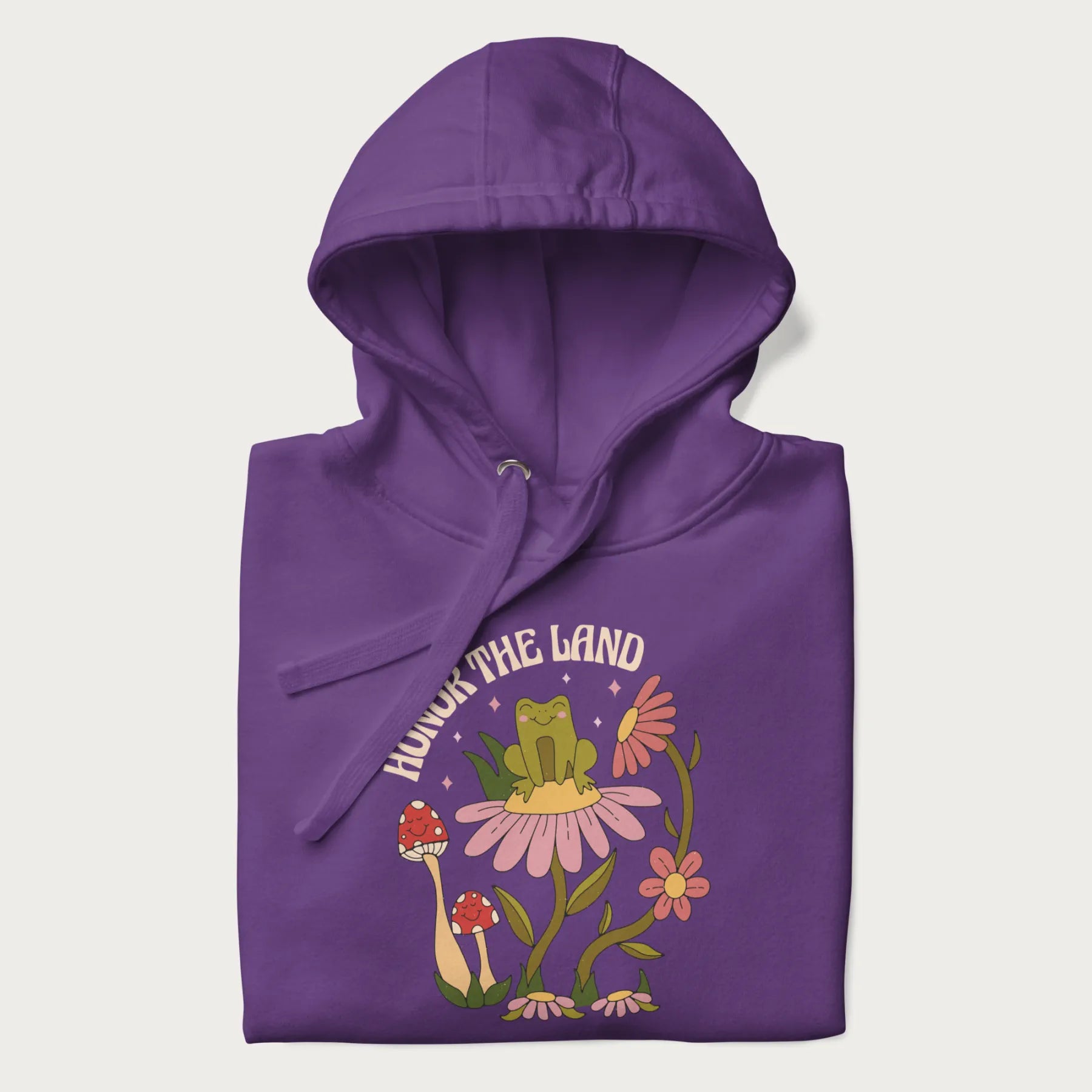 Folded purple hoodie with a graphic of a frog sitting on a flower, surrounded by mushrooms and flowers, with the text 'Honor the Land'.