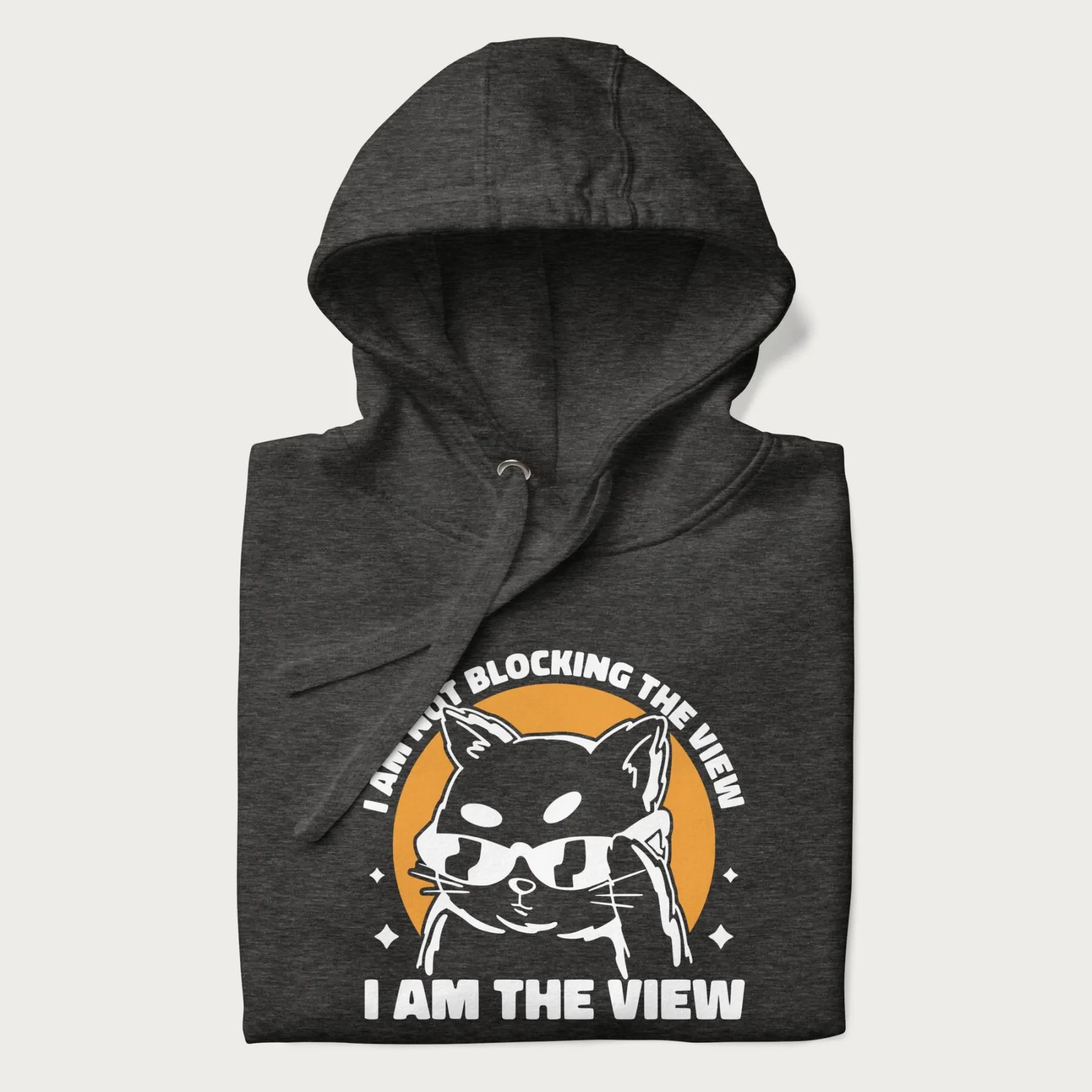 Folded dark grey hoodie with a confident cat wearing sunglasses and the phrase 'I am not blocking the view, I am the view'.