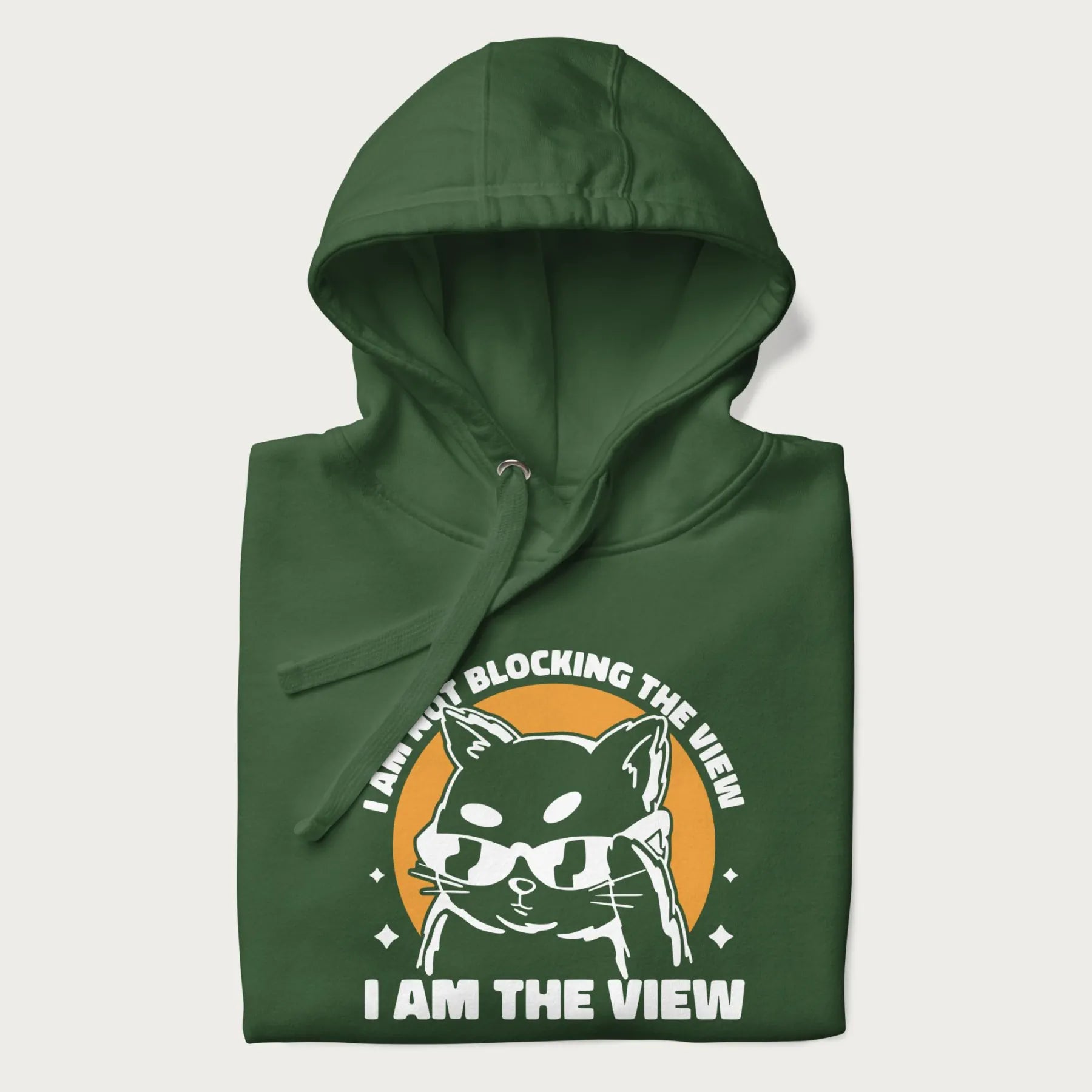 Folded green hoodie with a confident cat wearing sunglasses and the phrase 'I am not blocking the view, I am the view'.