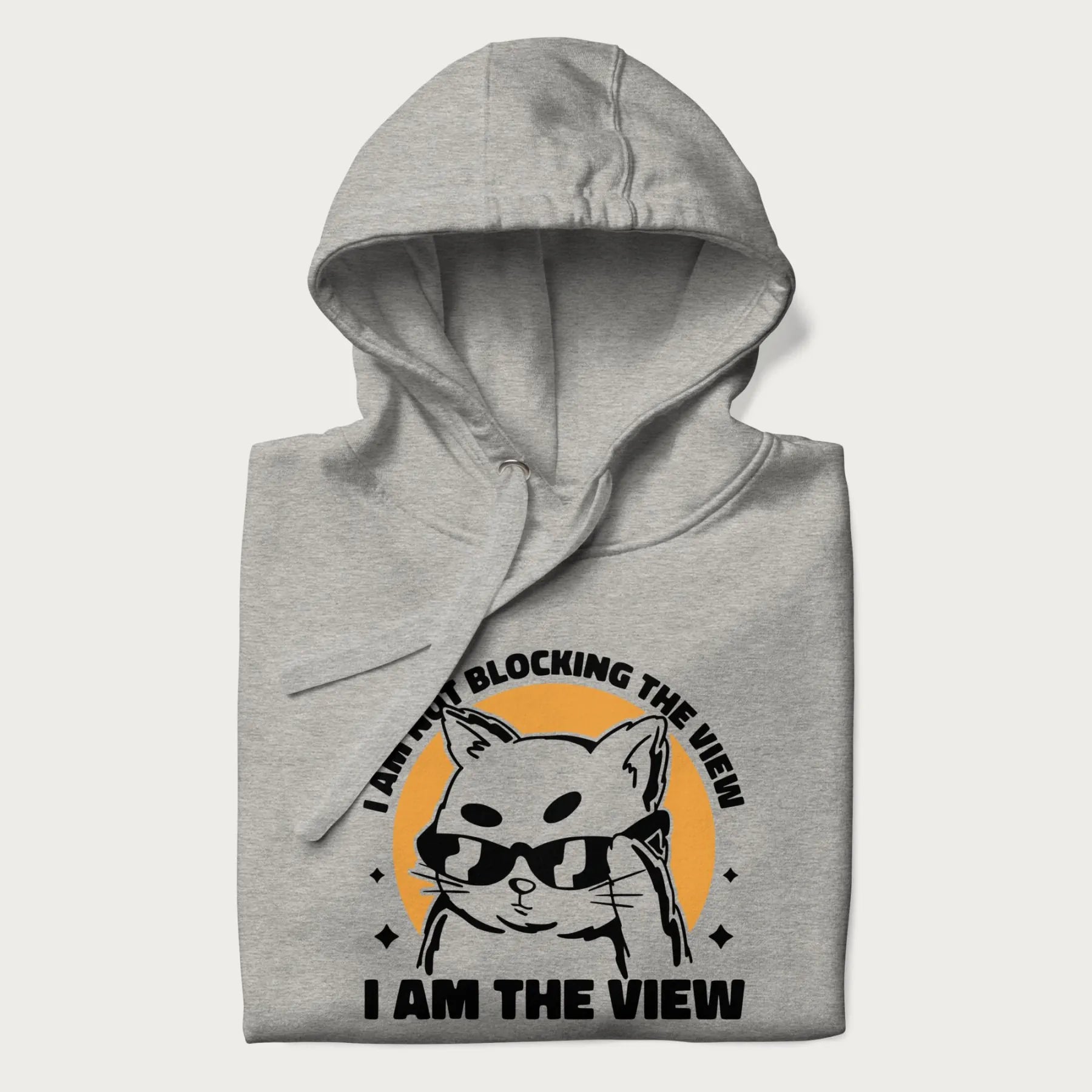 Folded light grey hoodie with a confident cat wearing sunglasses and the phrase 'I am not blocking the view, I am the view'.