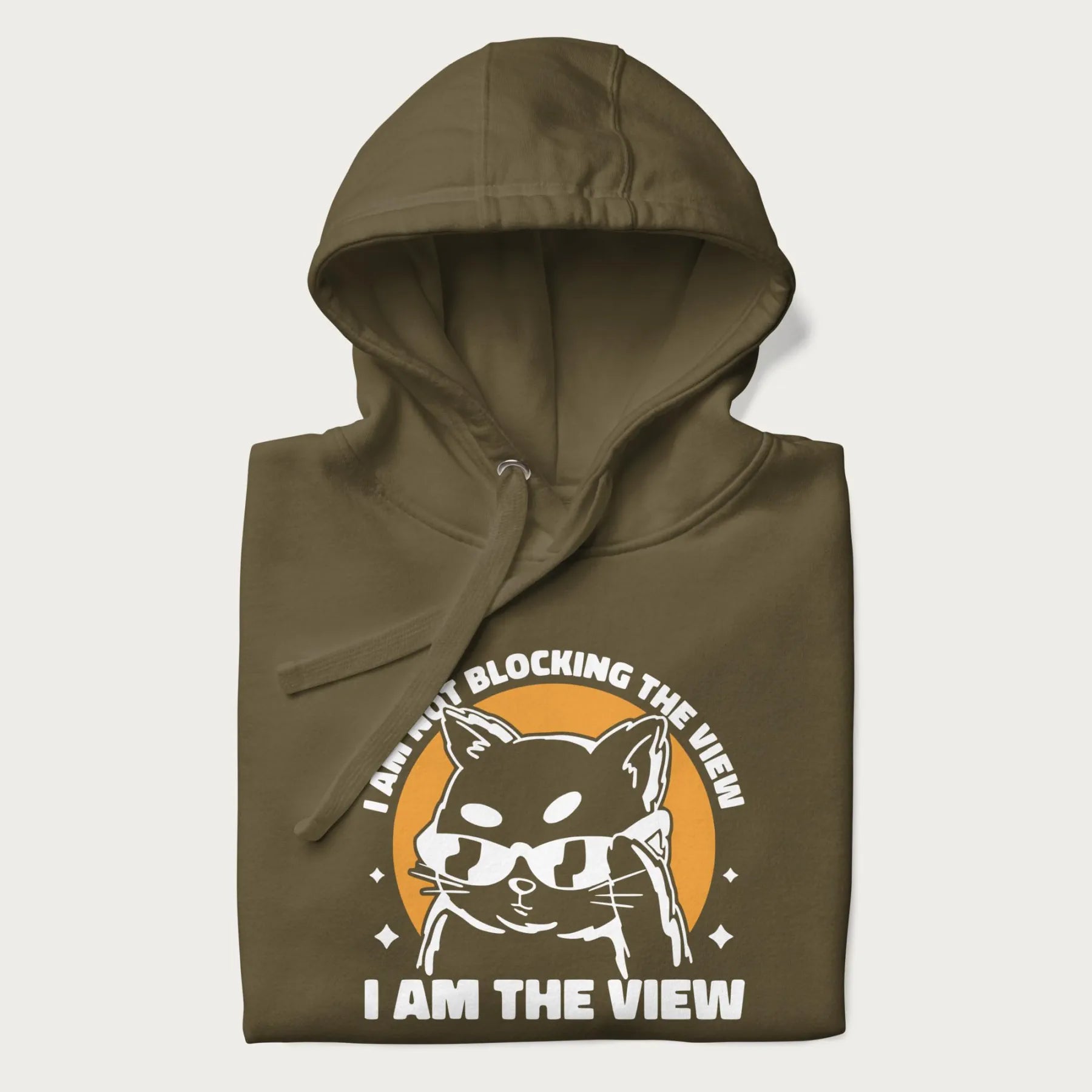 Folded military green hoodie with a confident cat wearing sunglasses and the phrase 'I am not blocking the view, I am the view'.