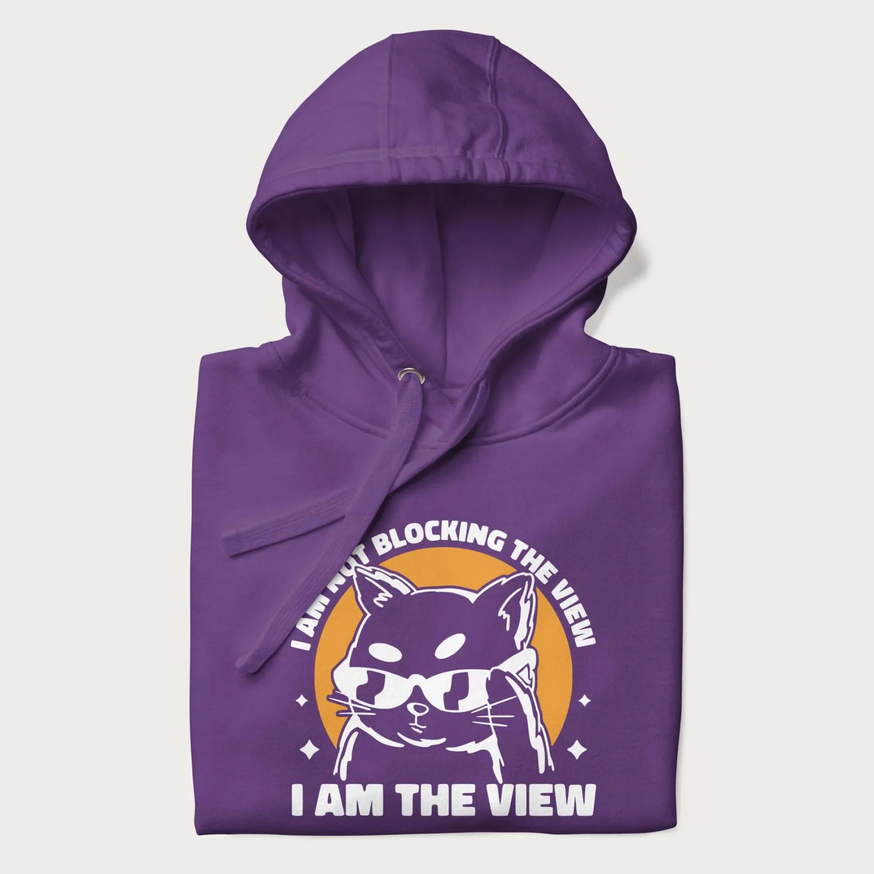 Folded purple hoodie with a confident cat wearing sunglasses and the phrase 'I am not blocking the view, I am the view'.