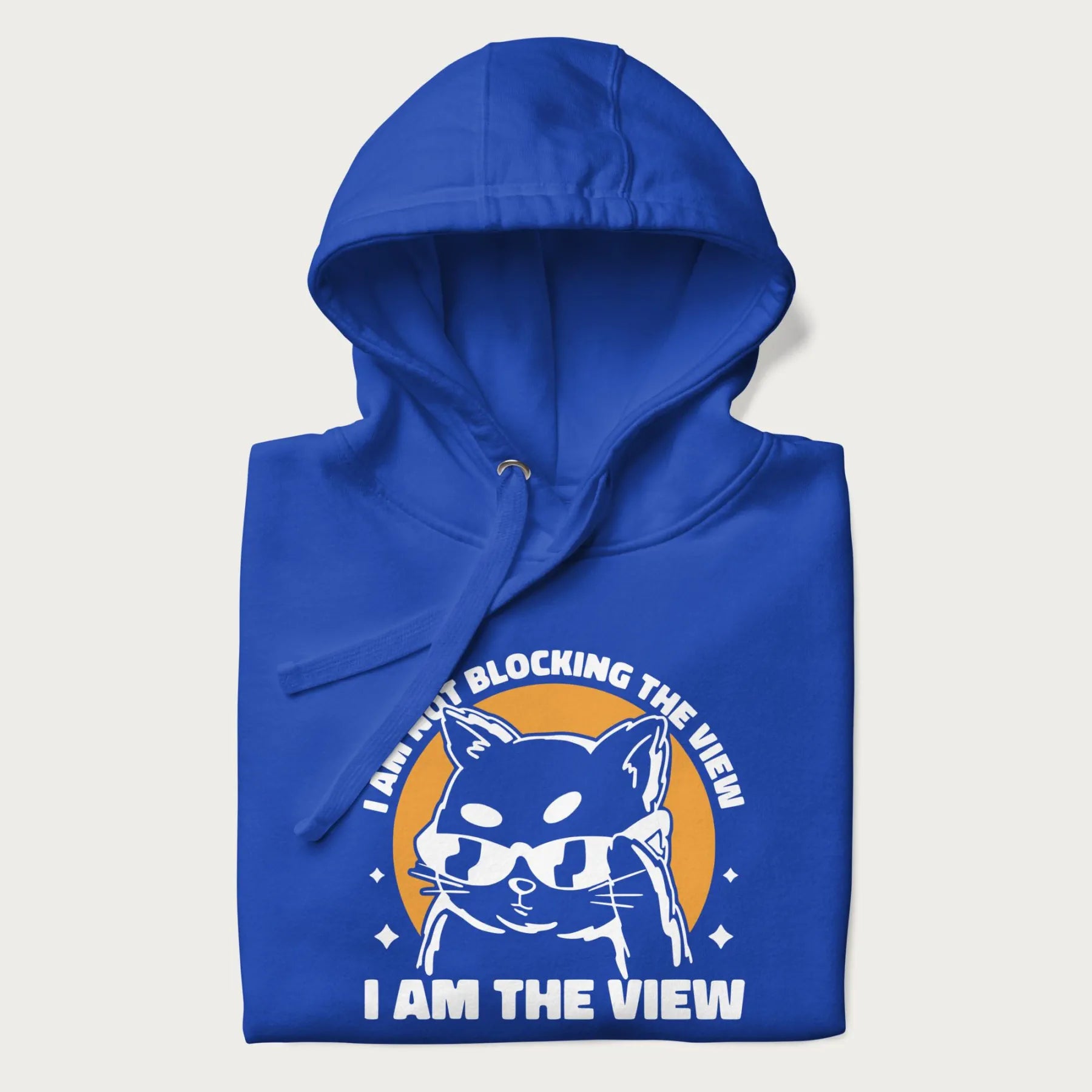 Folded royal blue hoodie with a confident cat wearing sunglasses and the phrase 'I am not blocking the view, I am the view'.