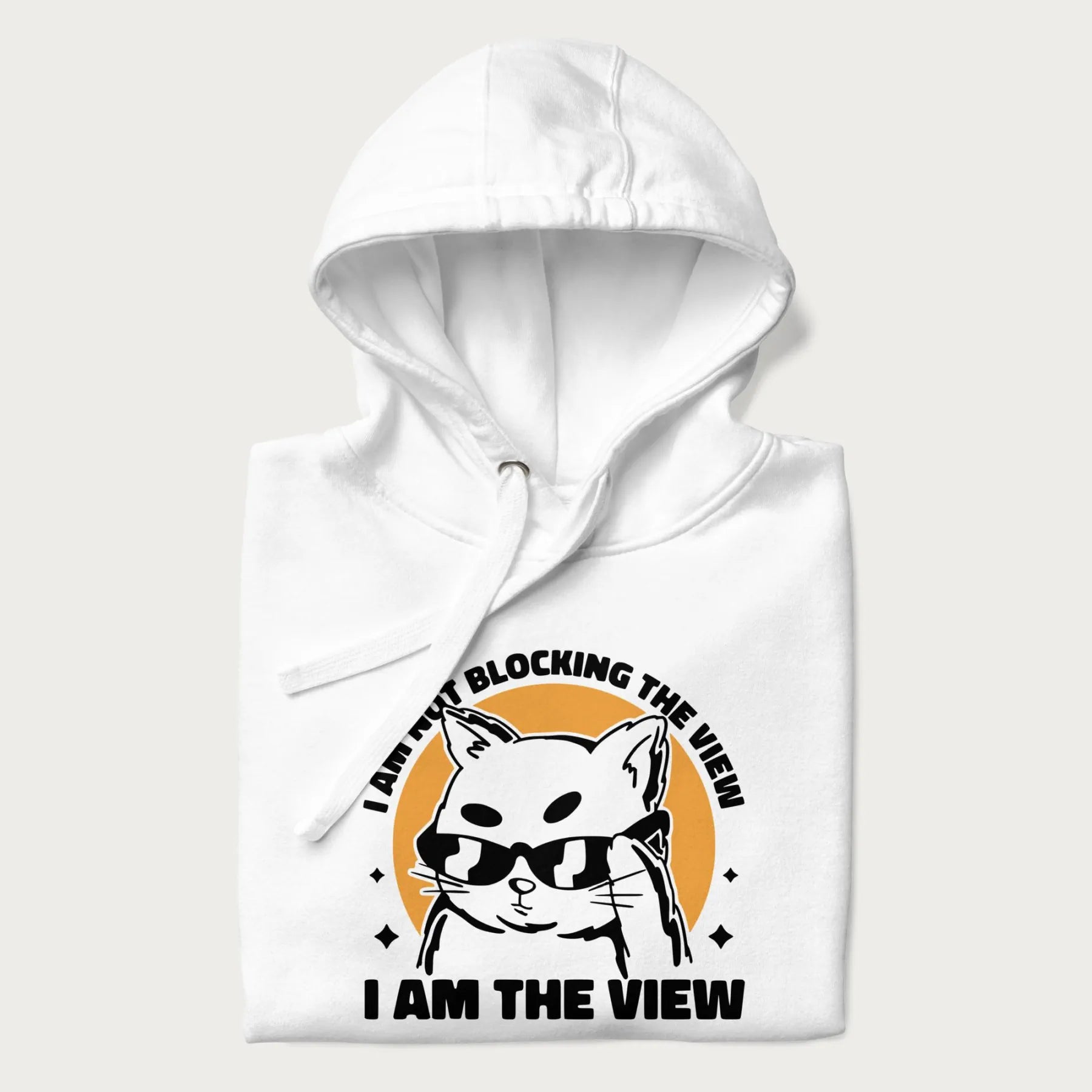 Folded white hoodie with a confident cat wearing sunglasses and the phrase 'I am not blocking the view, I am the view'.