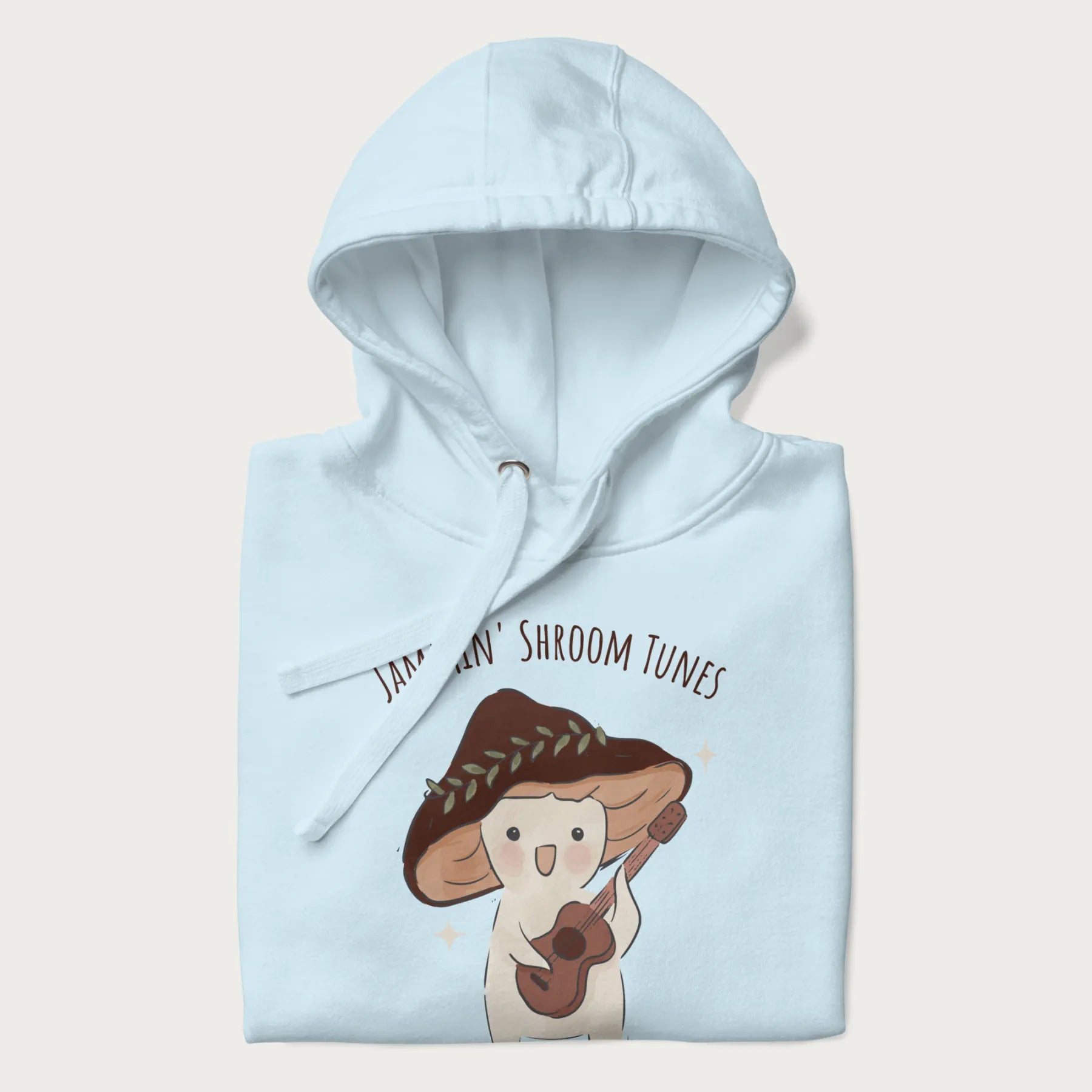 Folded light blue hoodie with a cute cottagecore mushroom character playing a guitar and the pun 'Jammin' Shroom Tunes' above.
