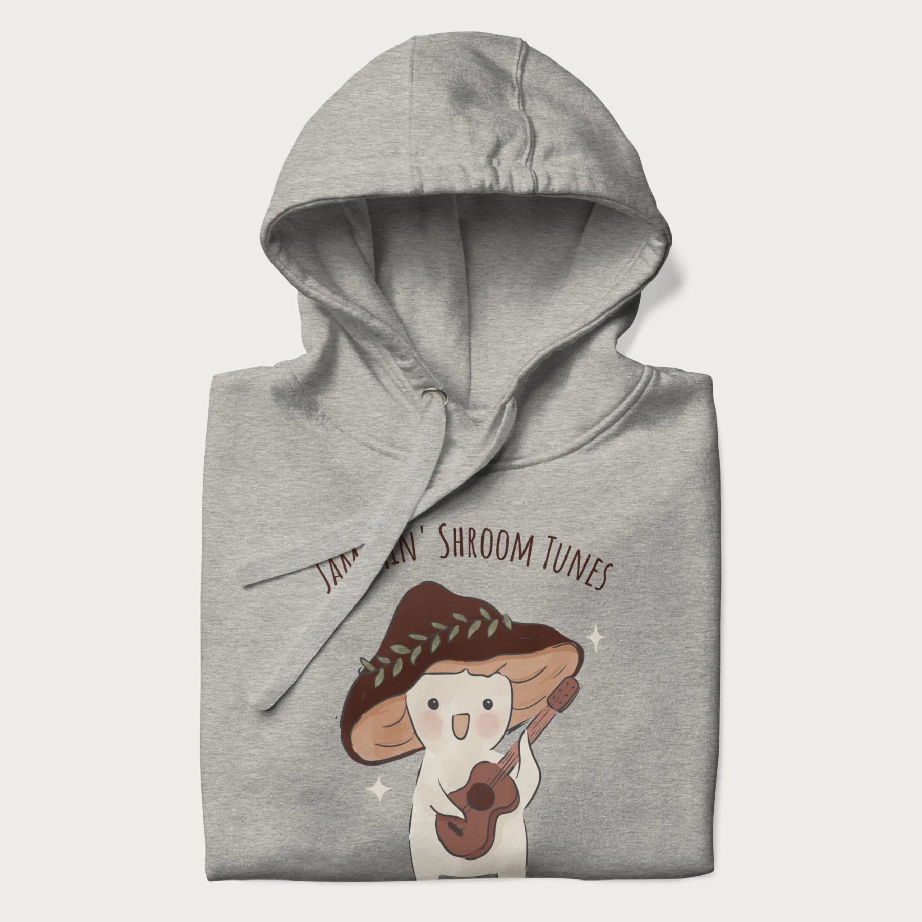 Folded light grey hoodie with a cute cottagecore mushroom character playing a guitar and the pun 'Jammin' Shroom Tunes' above.