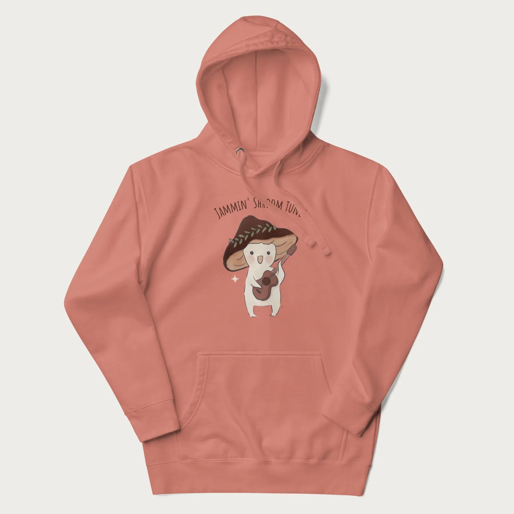 Light pink hoodie with a cute cottagecore mushroom character playing a guitar and the pun 'Jammin' Shroom Tunes' above.