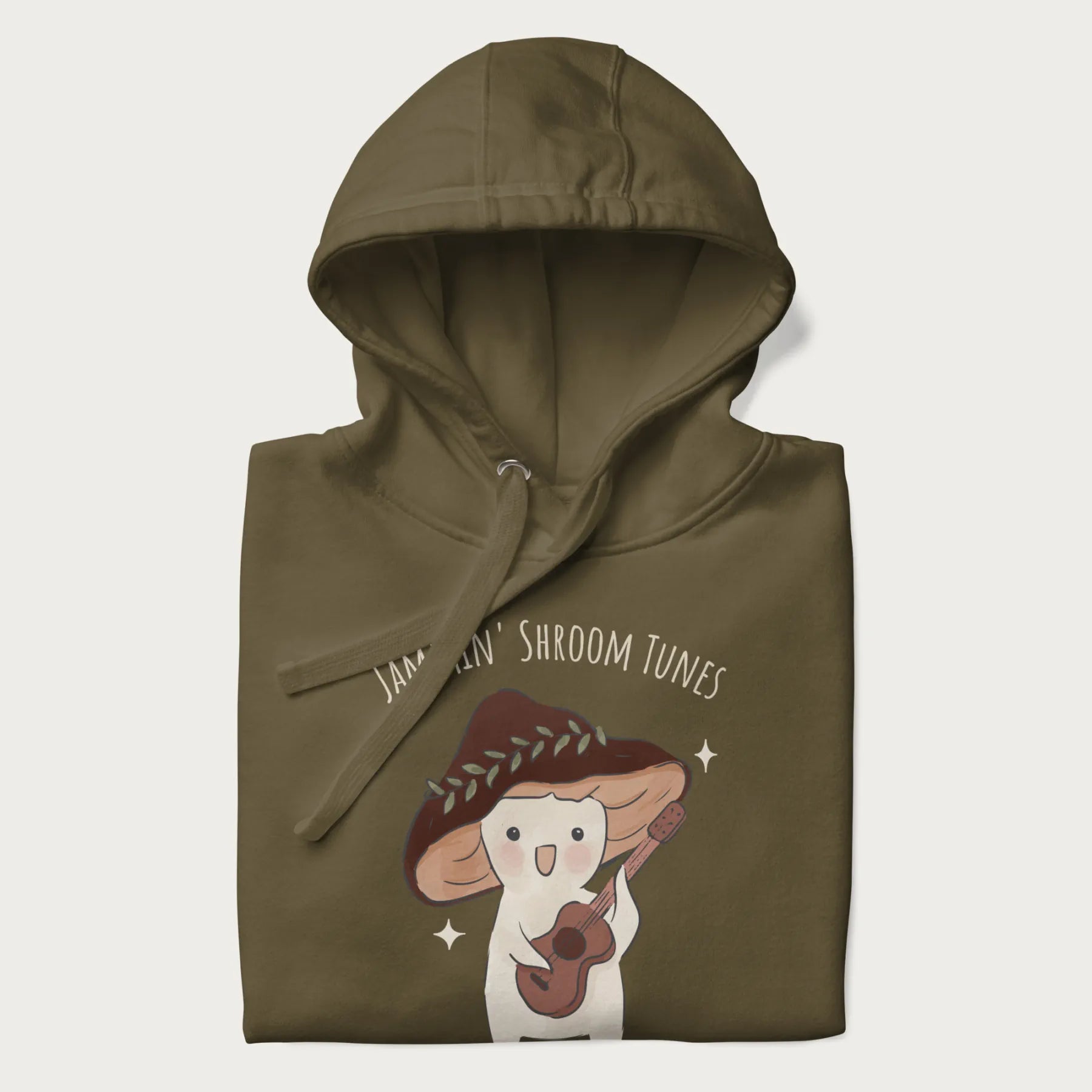 Folded military green hoodie with a cute cottagecore mushroom character playing a guitar and the pun 'Jammin' Shroom Tunes' above.