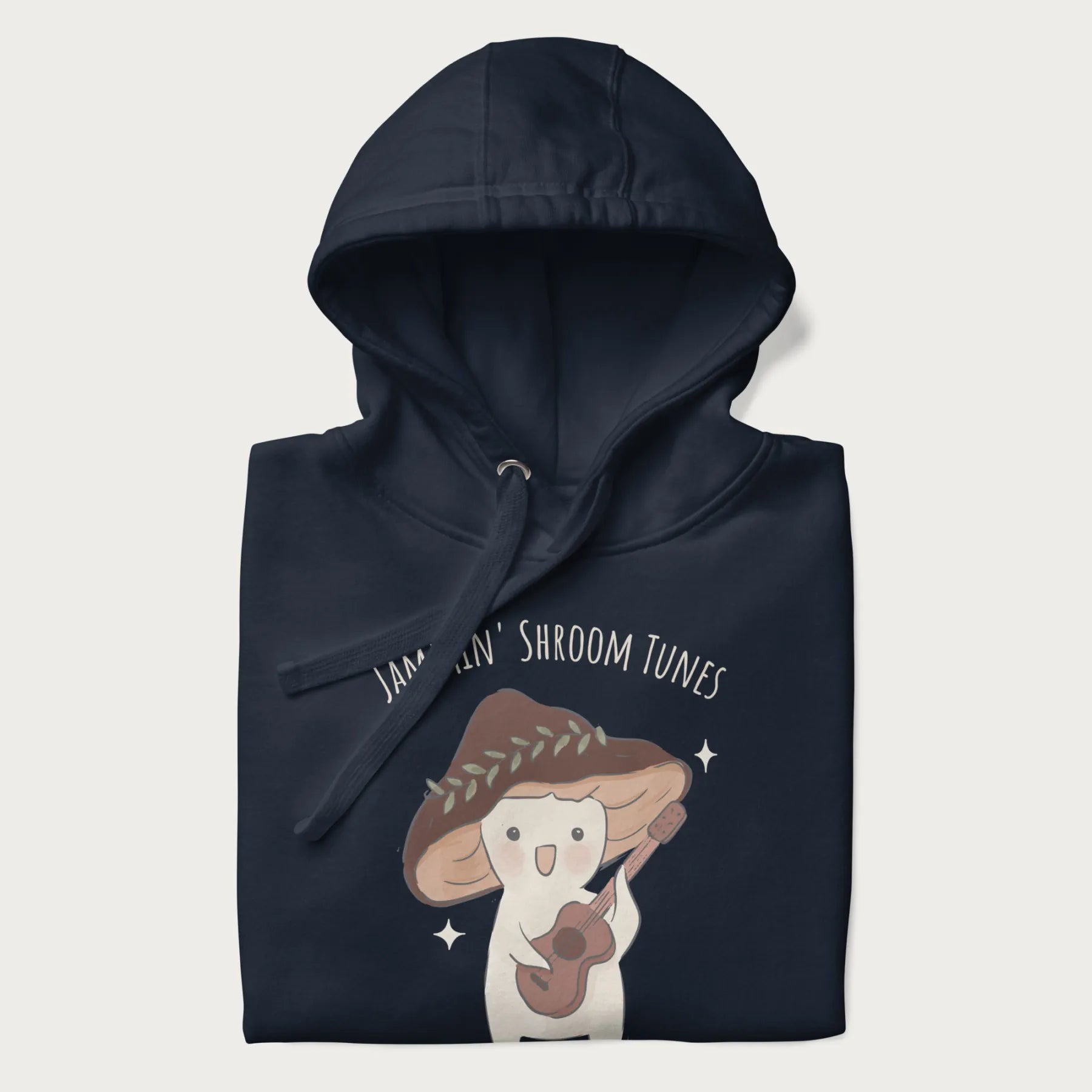 Folded navy blue hoodie with a cute cottagecore mushroom character playing a guitar and the pun 'Jammin' Shroom Tunes' above.