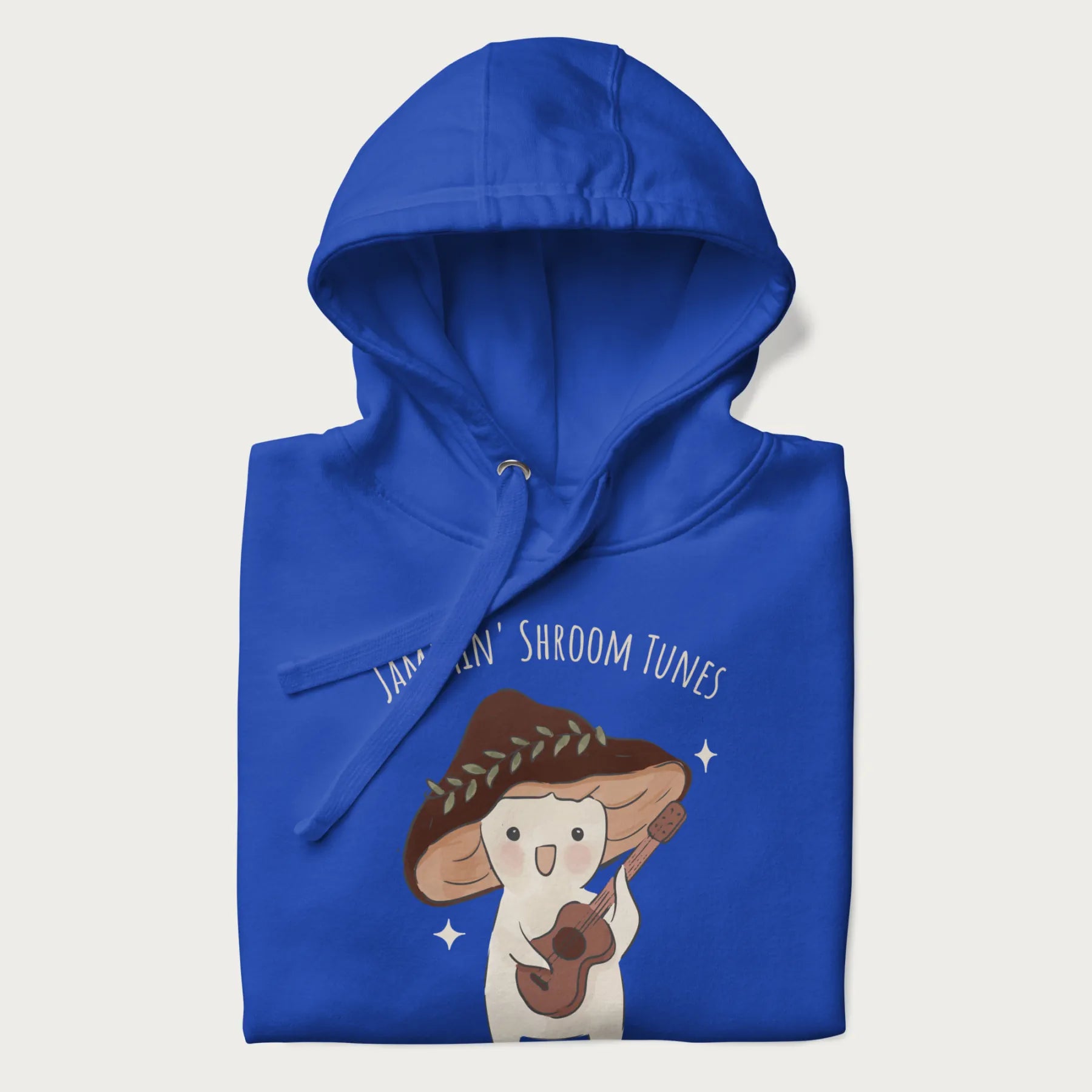 Folded royal blue hoodie with a cute cottagecore mushroom character playing a guitar and the pun 'Jammin' Shroom Tunes' above.