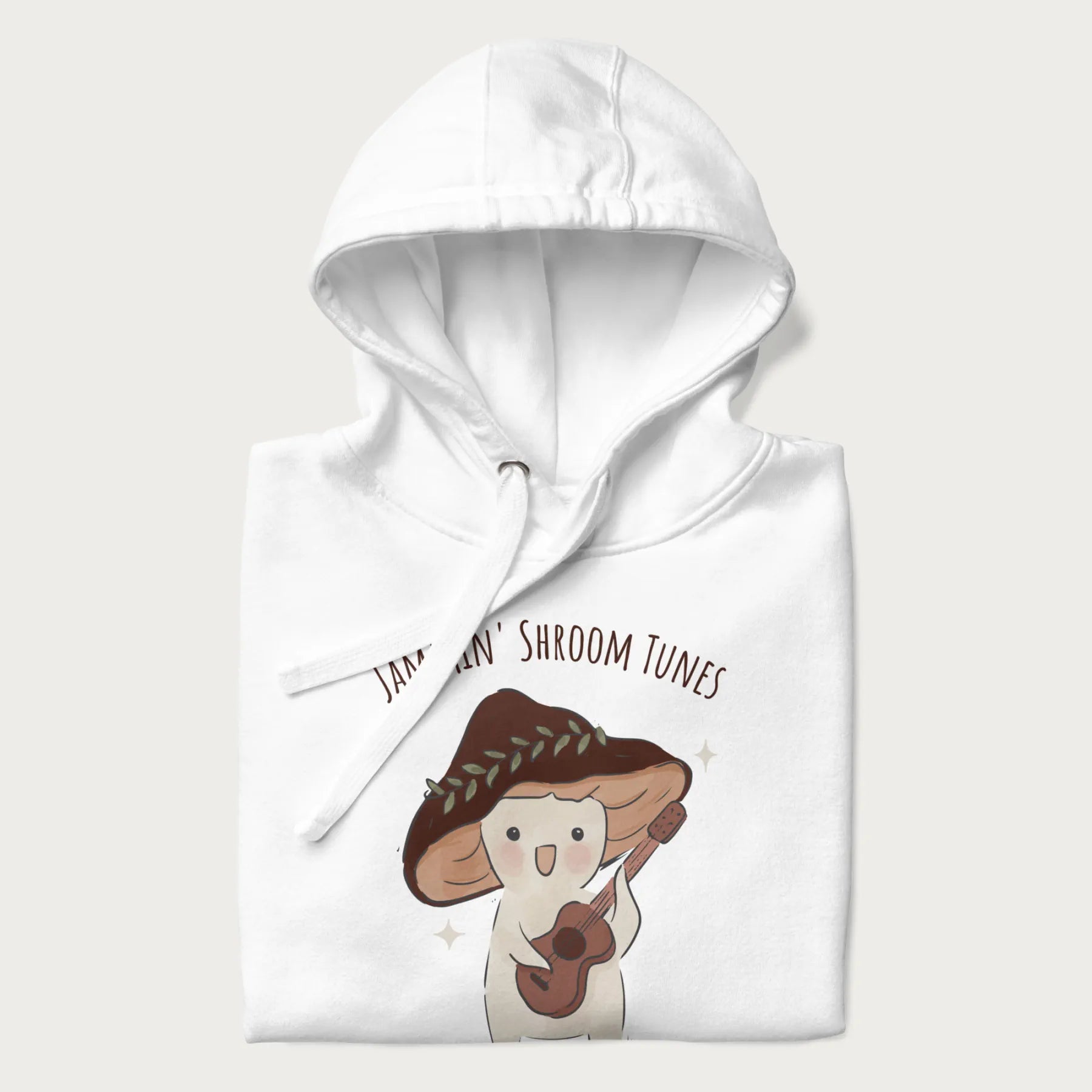 Folded white hoodie with a cute cottagecore mushroom character playing a guitar and the pun 'Jammin' Shroom Tunes' above.