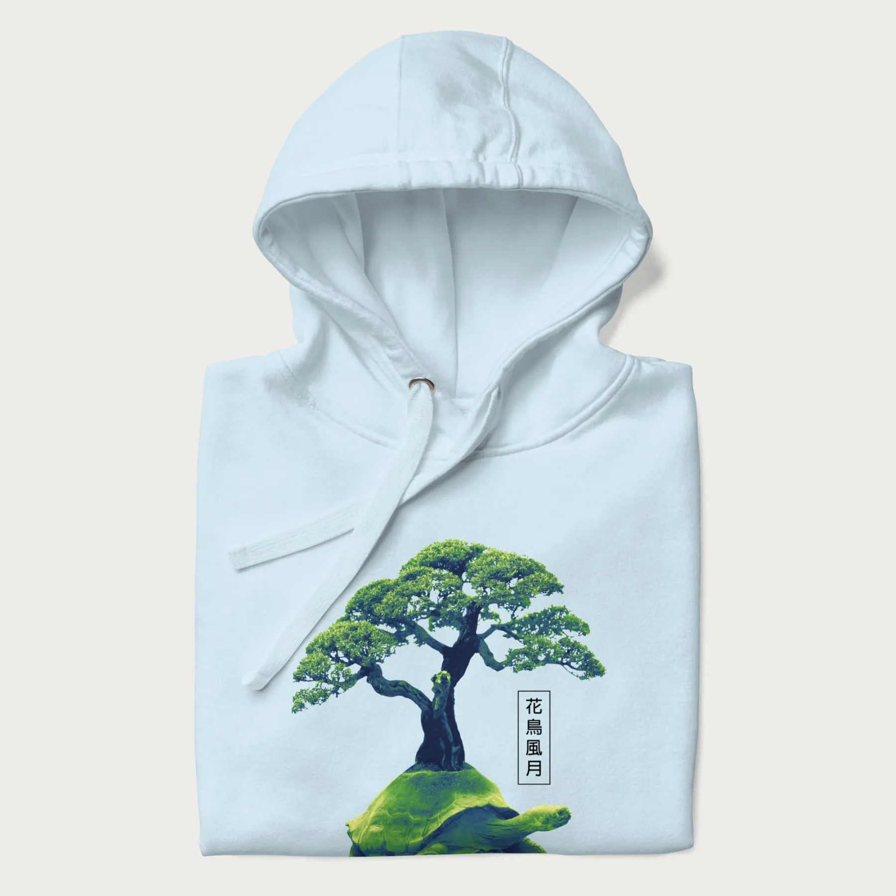 Folded light blue hoodie with a vibrant graphic of a turtle carrying a bonsai tree and Japanese text '花鳥風月.'