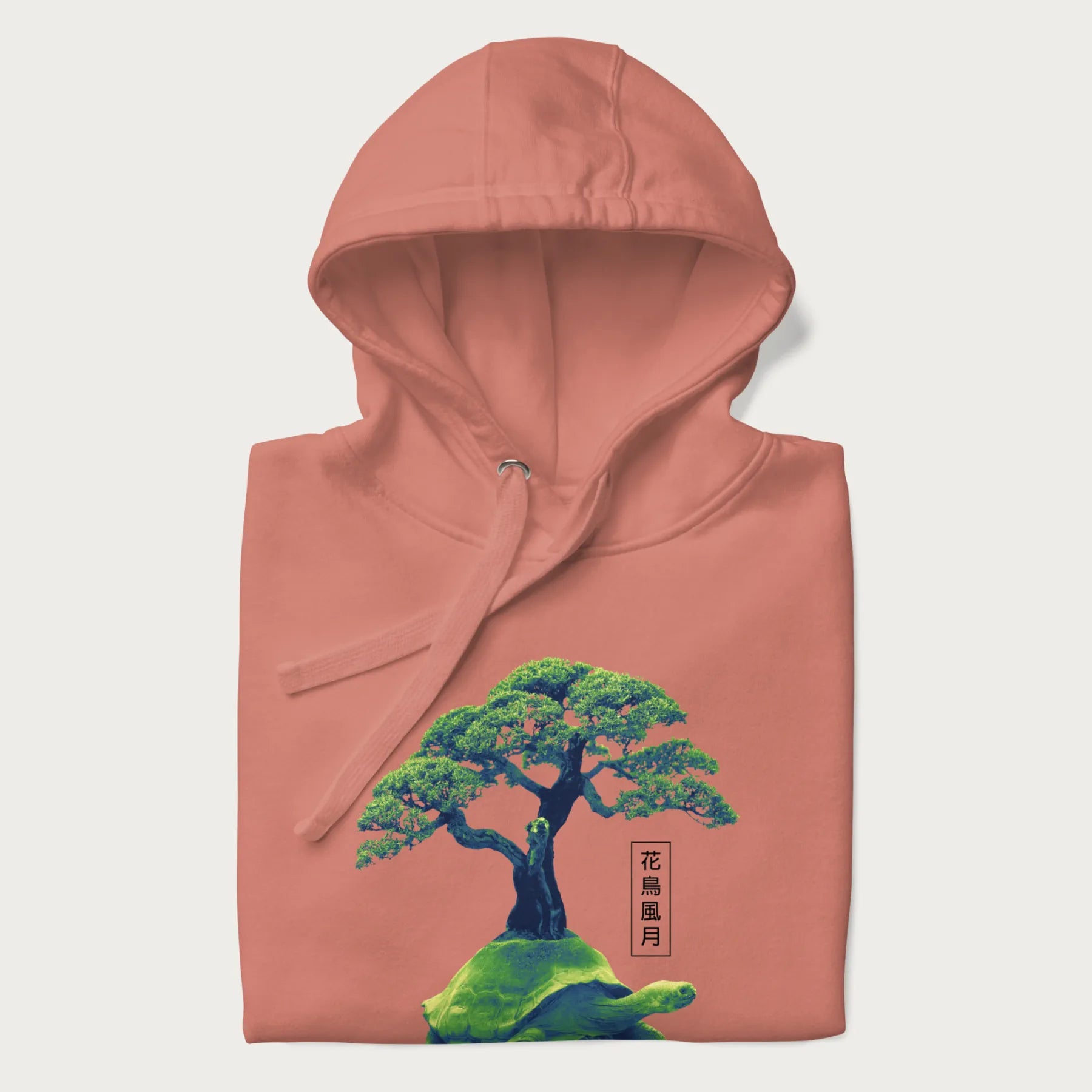 Folded light pink hoodie with a vibrant graphic of a turtle carrying a bonsai tree and Japanese text '花鳥風月.'